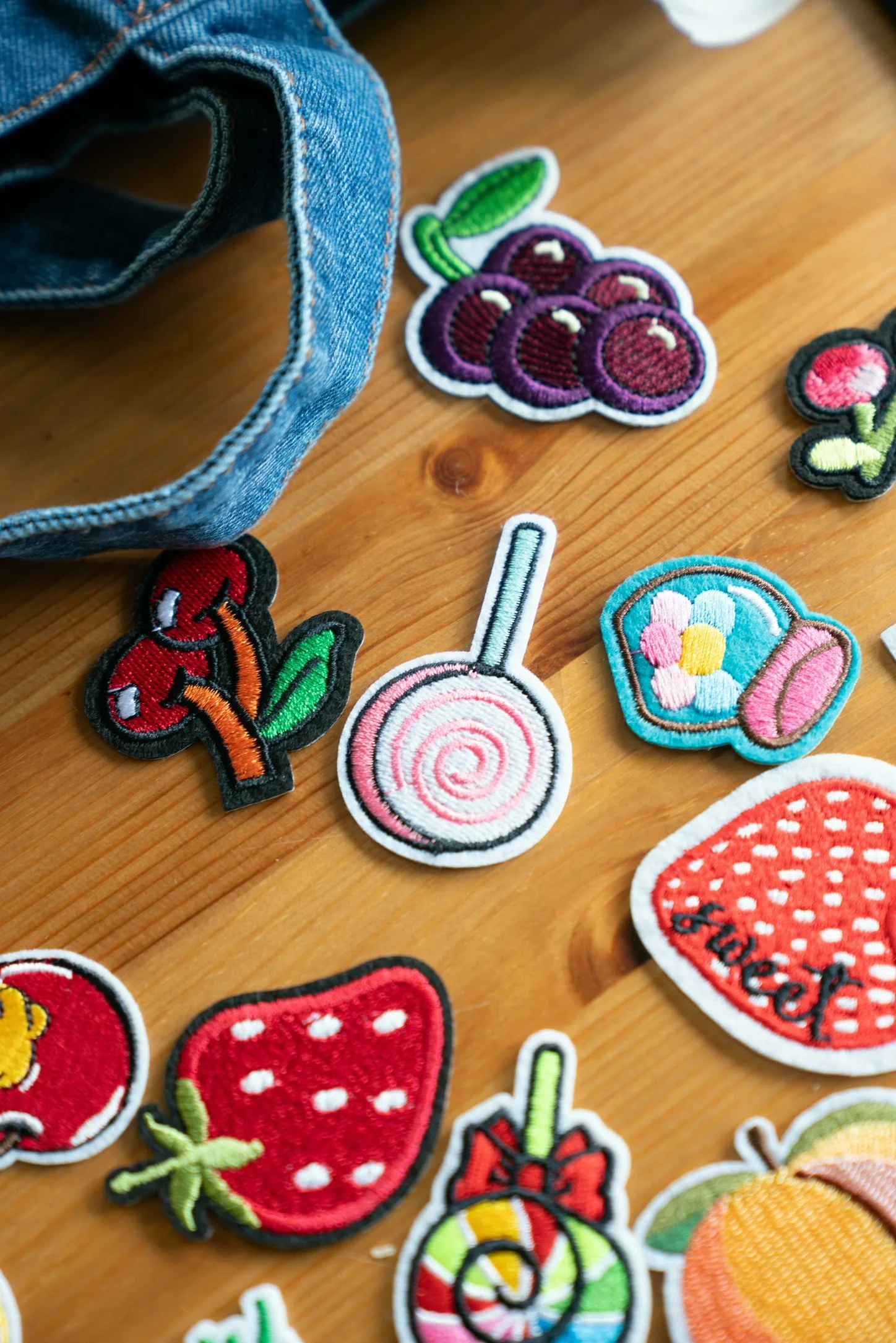 Close-up of various embroidered patches on a wooden surface, including cherries, strawberries, a lollipop, and other colorful designs.