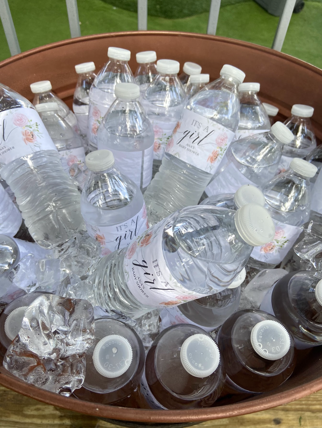 A large container filled with bottled water with labels that say "It's a girl" for a baby shower, surrounded by ice.