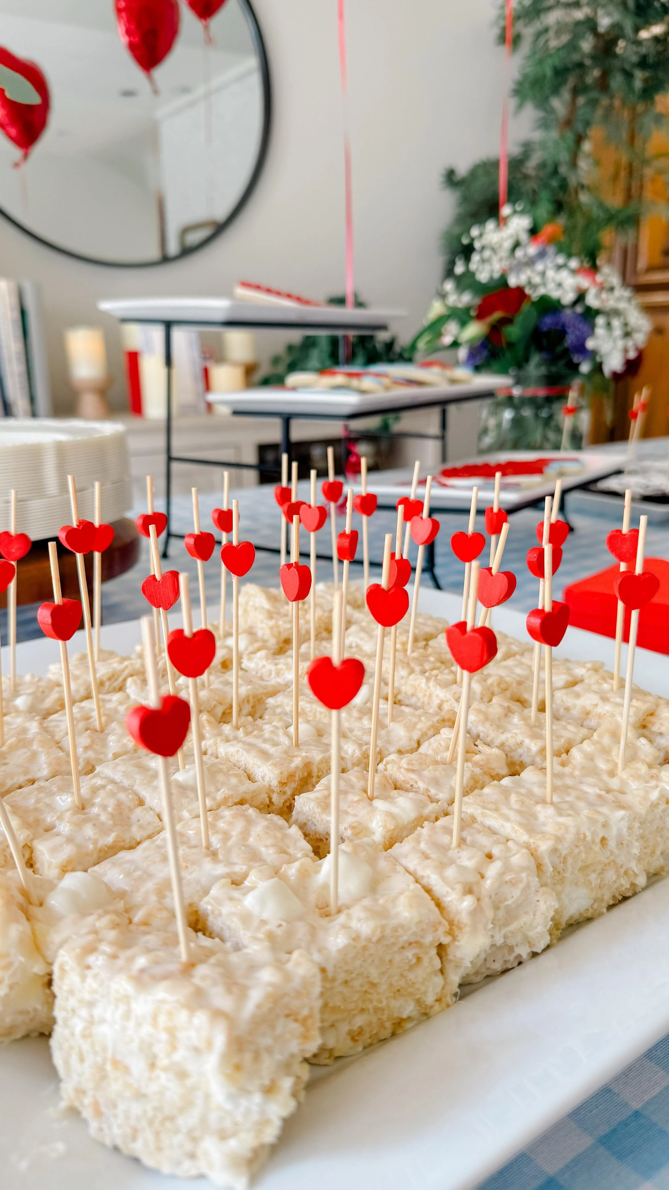 Buffalo chicken dip with cheese, topped with small red heart-shaped toothpicks, at a celebration table with Valentine's Day decorations.