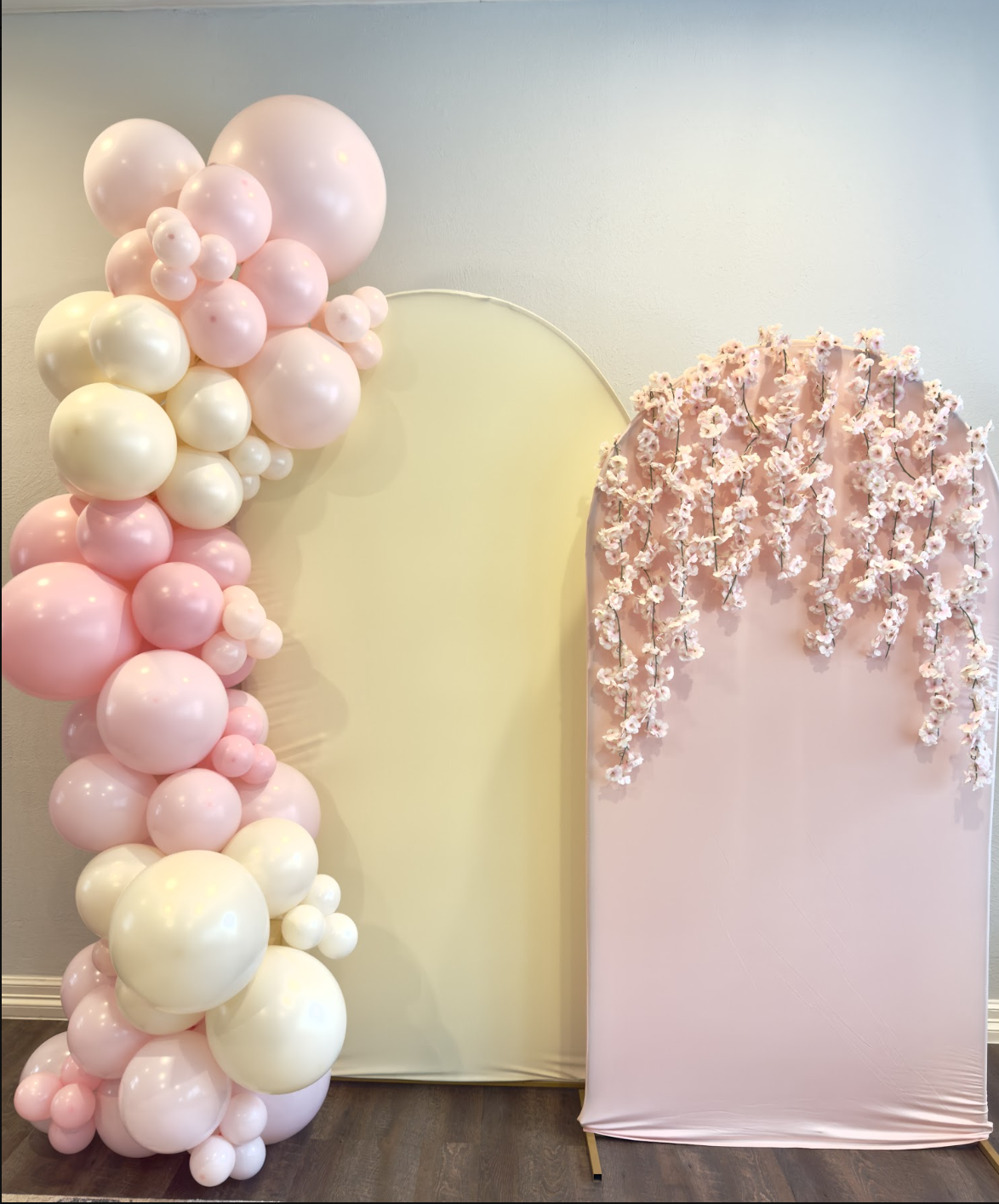 Decorative backdrop with pink and white balloon arrangement on the left and a pink fabric panel with hanging white flowers on the right.