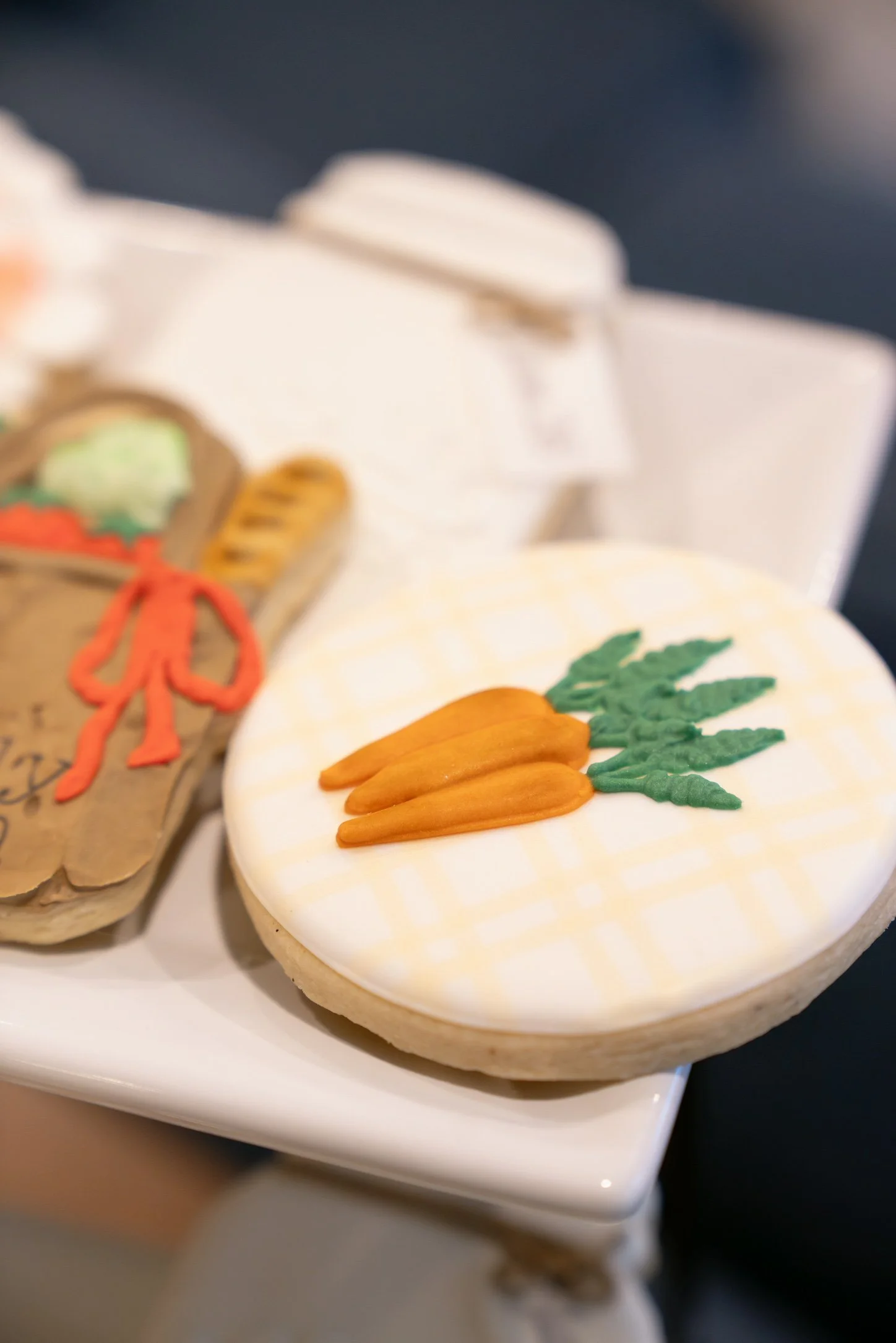 Decorative cookies on a white plate, featuring a carrot and green leaves in icing.