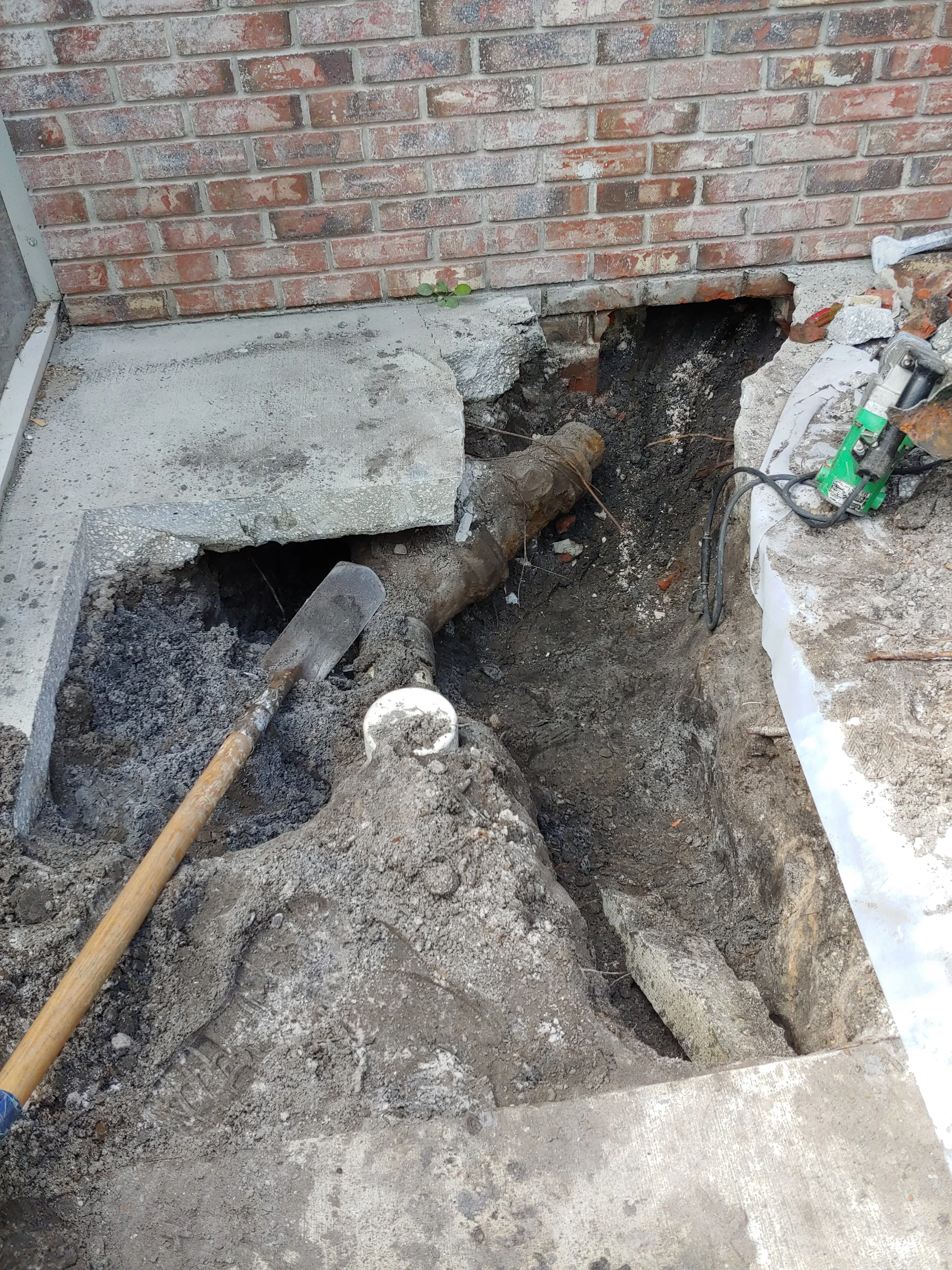 Construction site with exposed underground pipe, debris, and a brick wall.