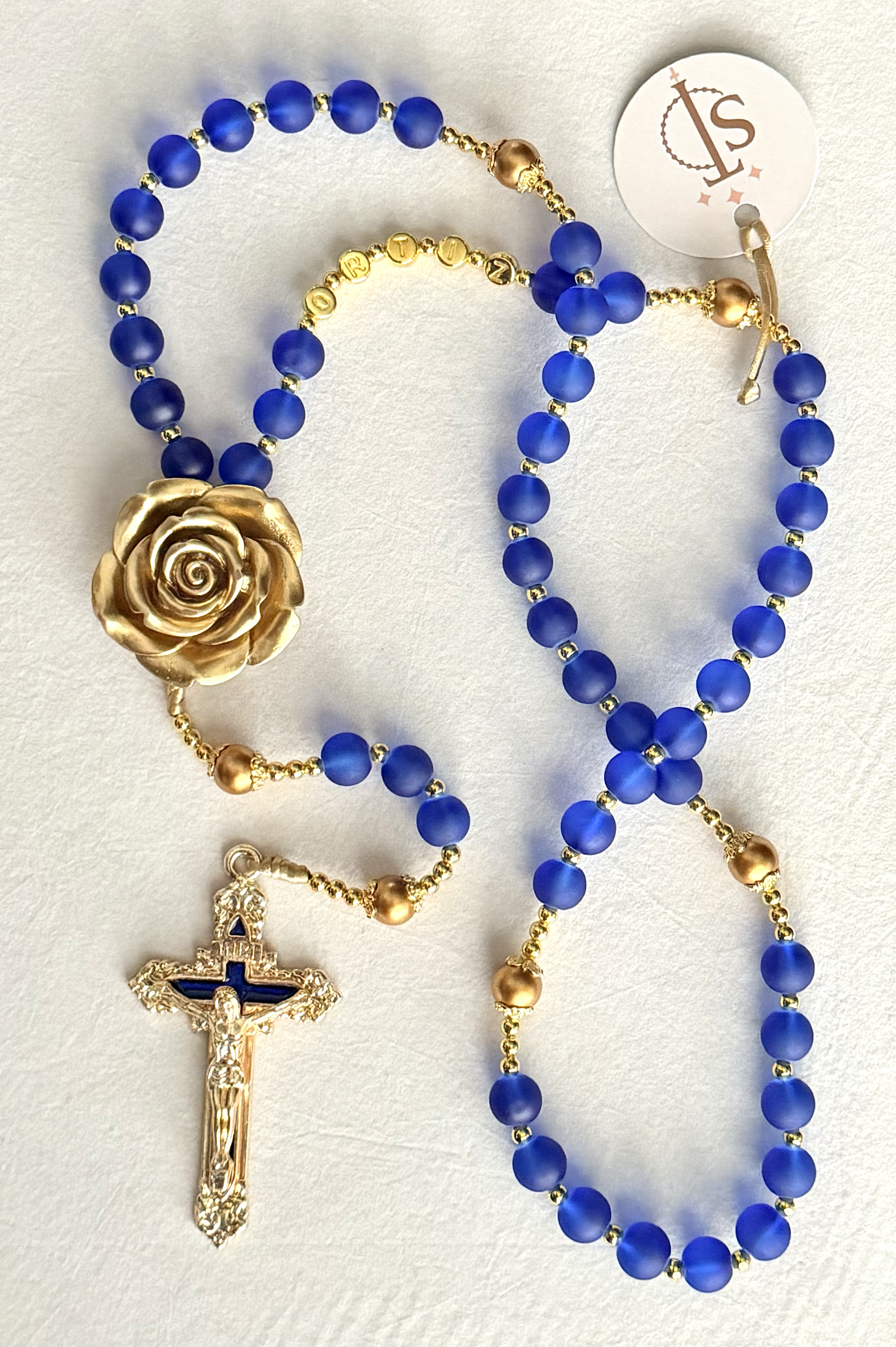 Blue beaded rosary with a gold flower centerpiece and a gold crucifix.