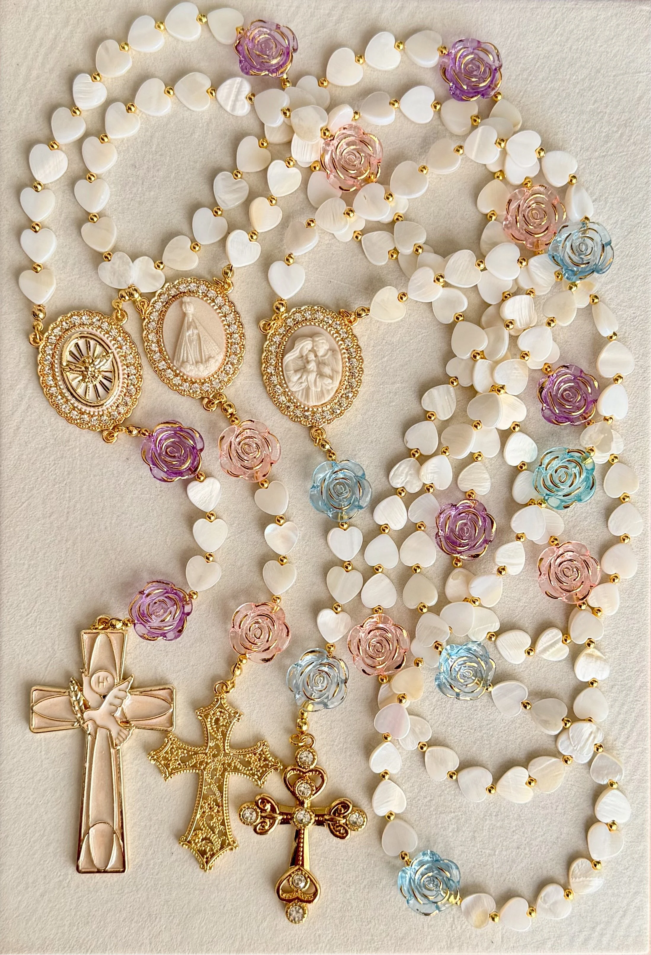 Collection of Holy Communion necklaces featuring various religious medals and rosaries with pearl and colored bead accents, displayed on a light fabric background.