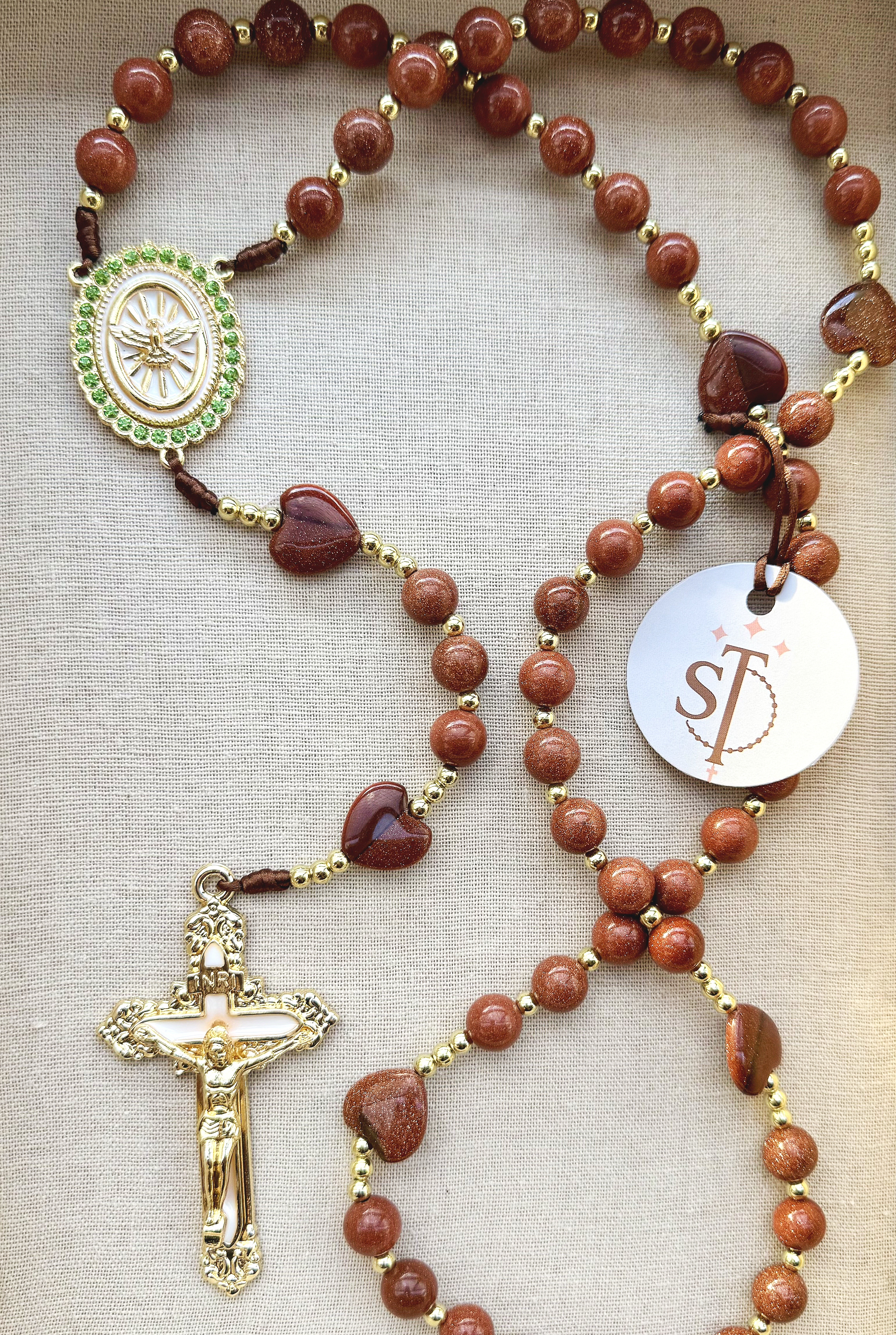 Brown beaded rosary with gold accents, featuring a gold crucifix with detailed design and a circular medallion with green accents.
