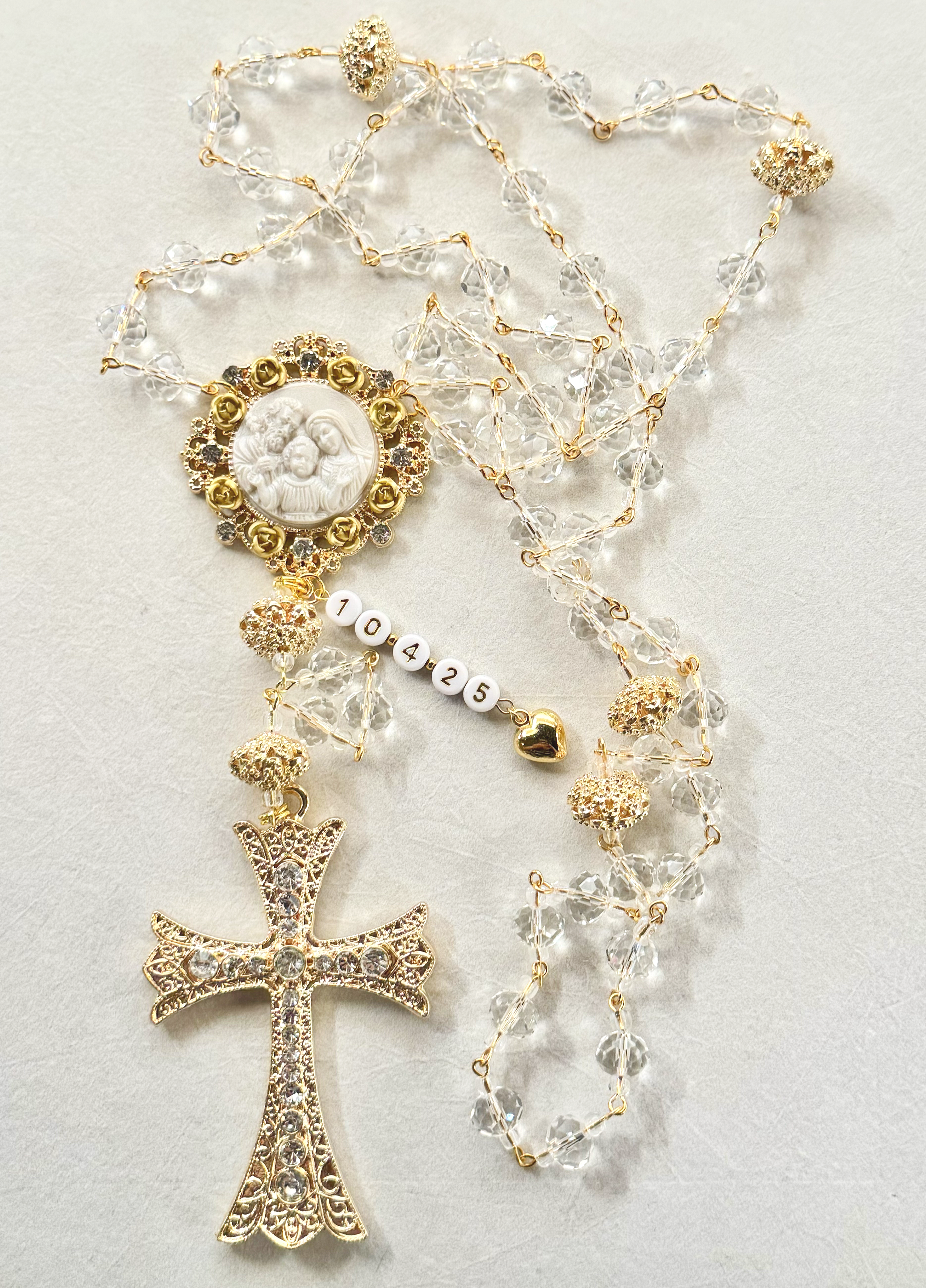 Gold and crystal jewelry with a religious pendant, crosses, and beads, laid out on a light surface.