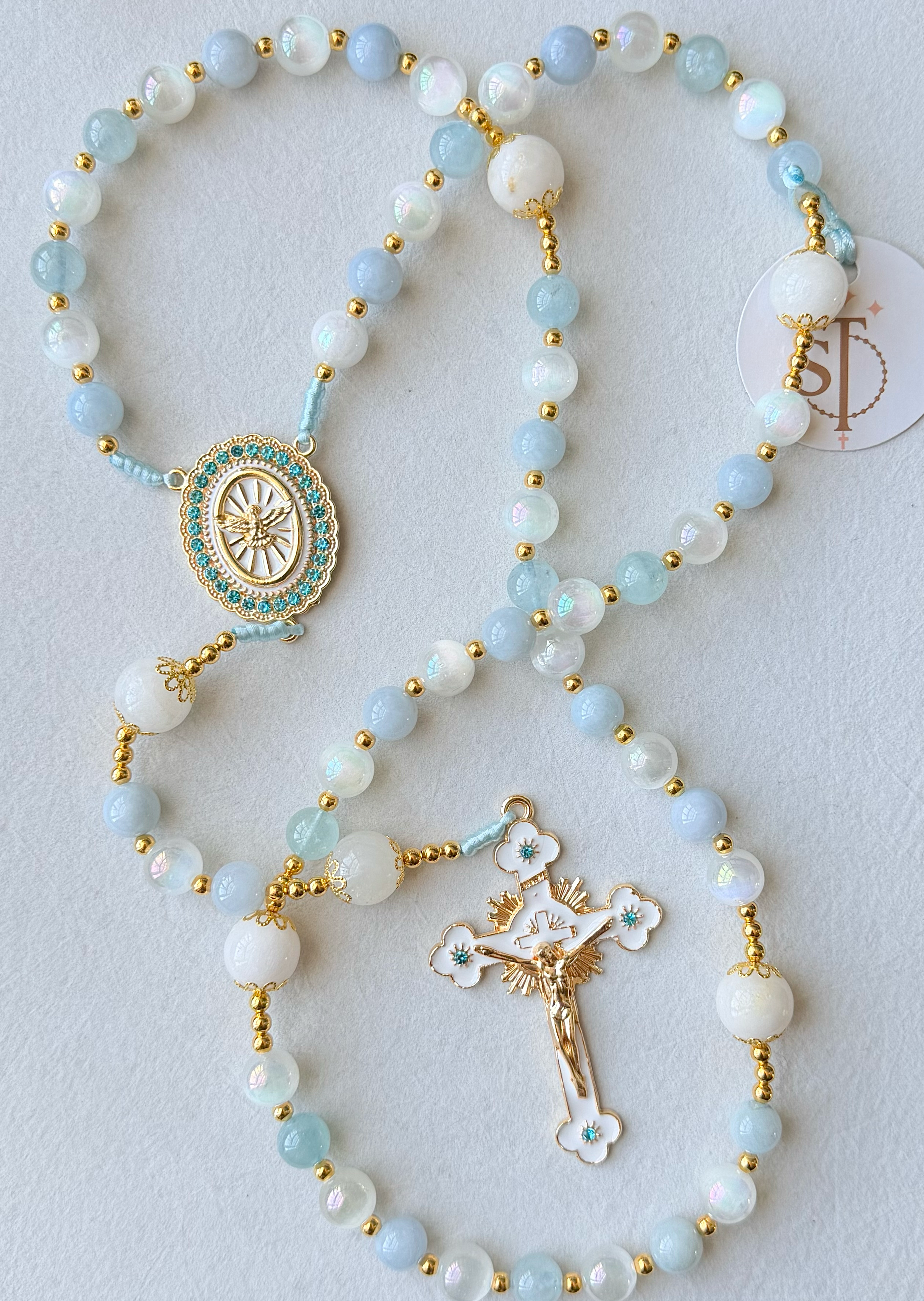 A collection of beaded necklaces with gold accents, featuring religious and decorative pendants, laid out on a white surface.
