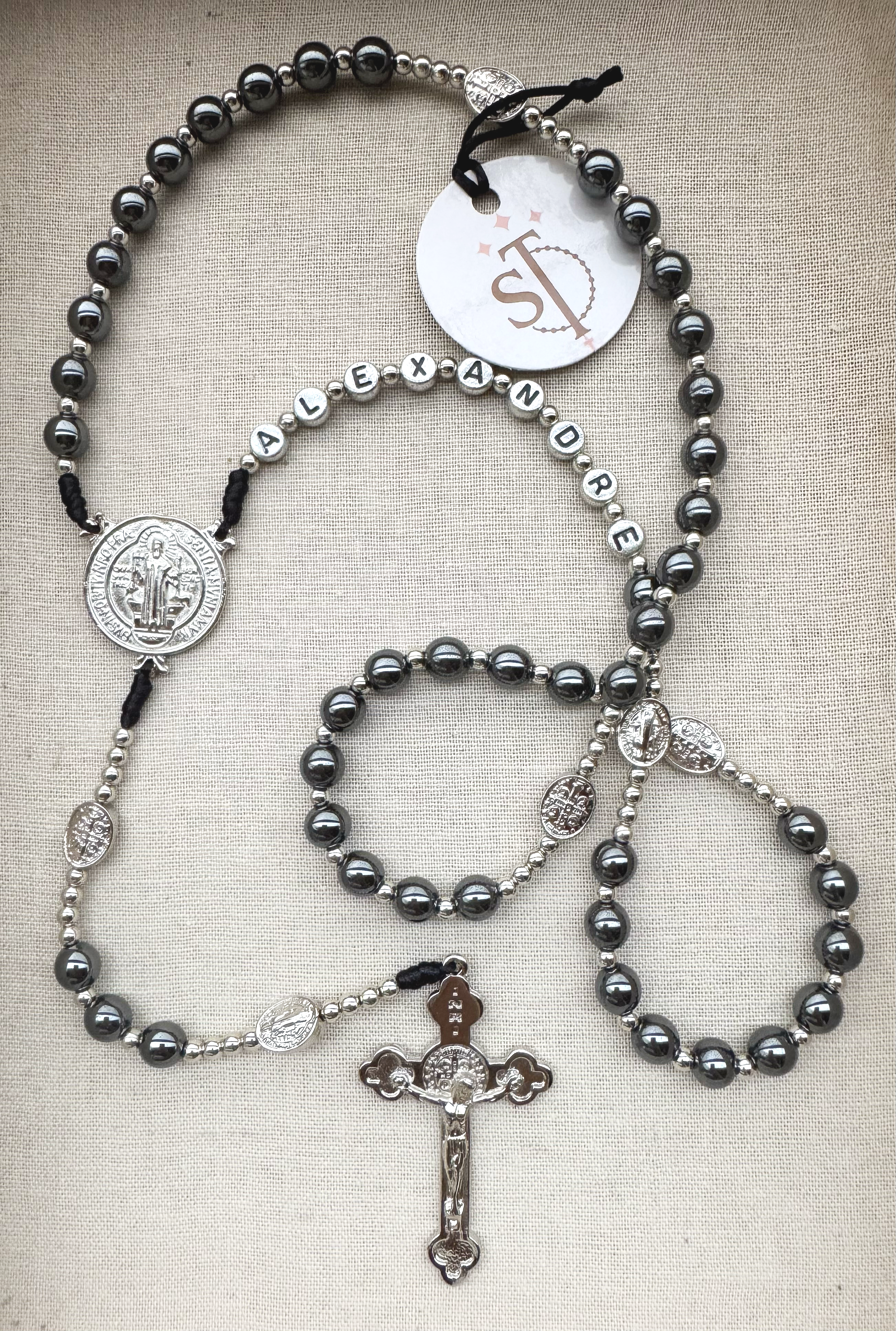 Various Catholic rosary necklaces with beads and medals, laid out on a beige fabric background.