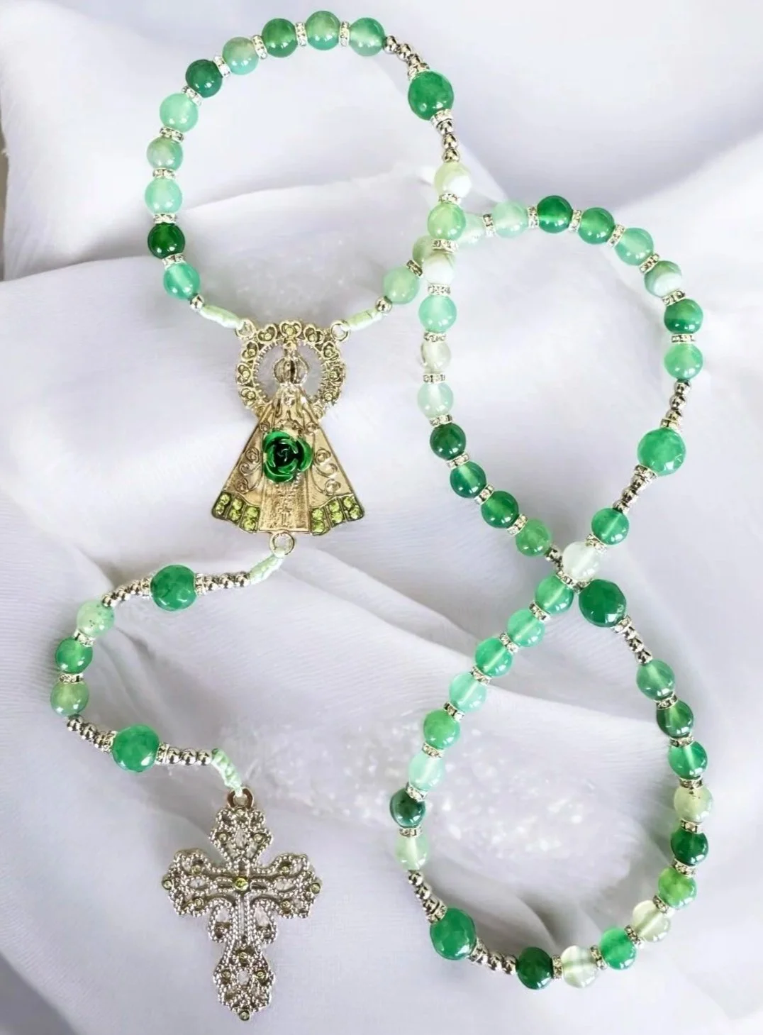 Green beaded religious rosary necklace with a silver cross and a medal featuring the Virgin Mary.
