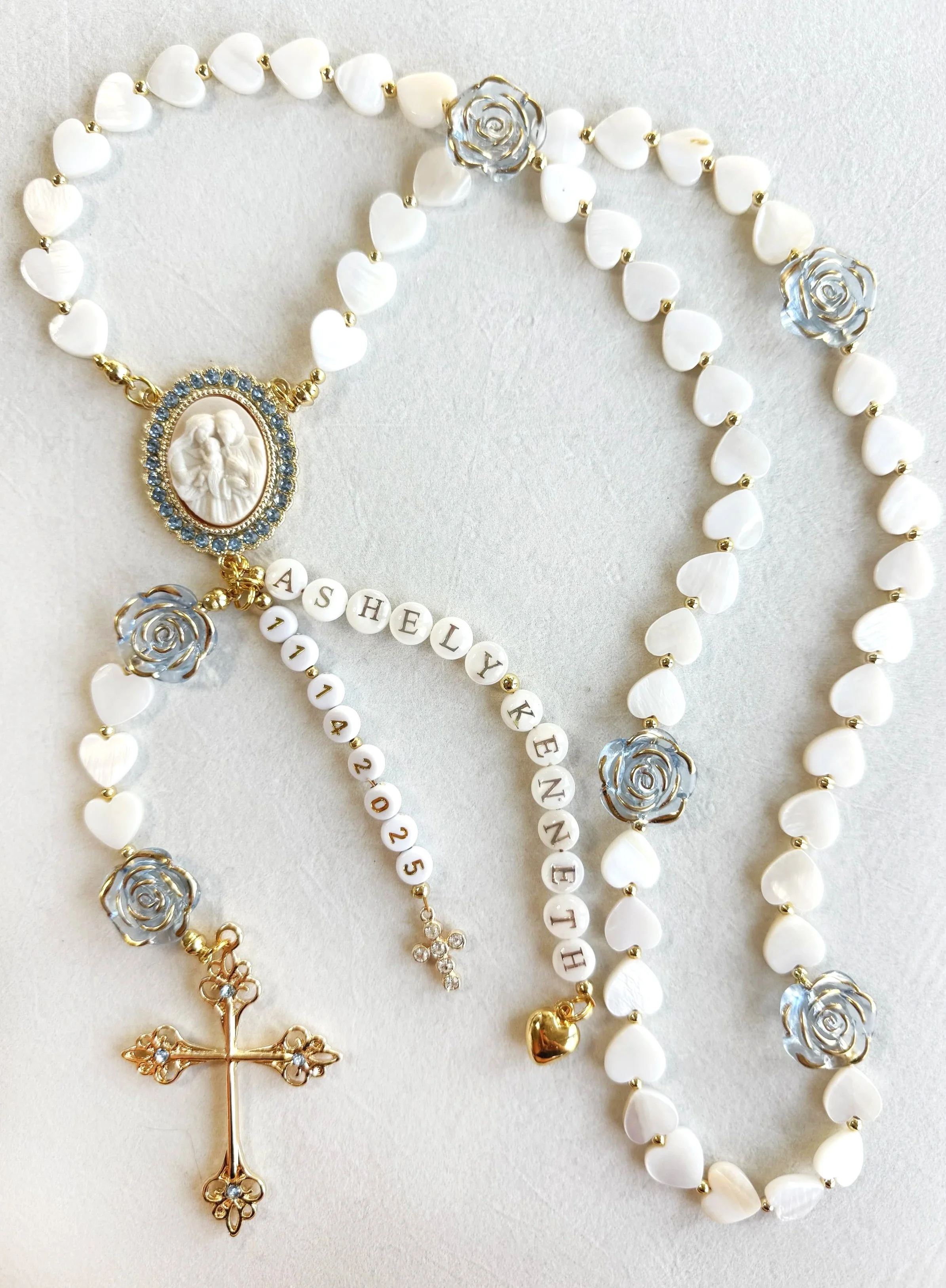 Multiple white beaded necklaces with gold accents, featuring roses, hearts, a cross, and the name 'Ashley' spelled with letter beads.