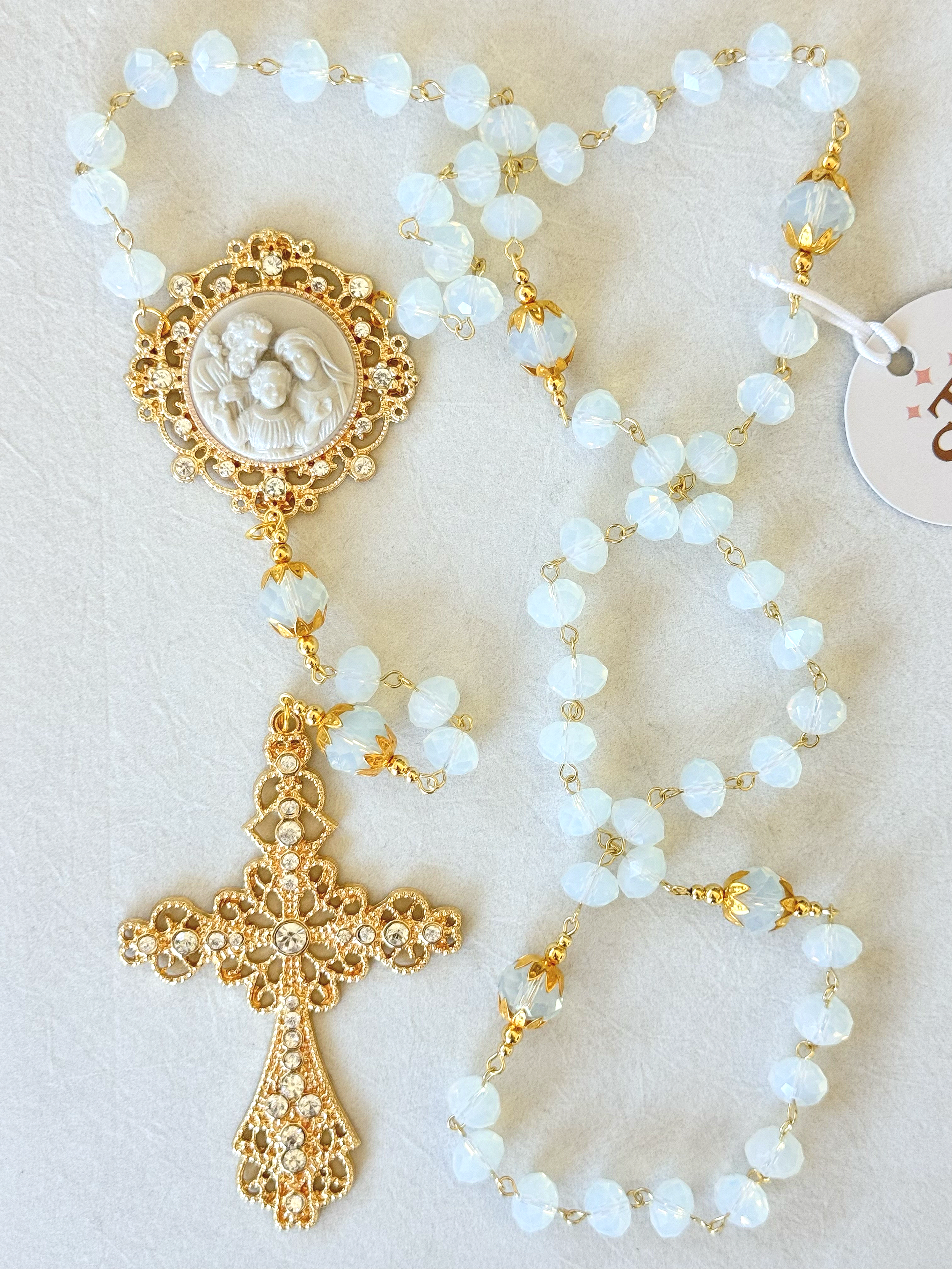 Gold and white rosary with a crucifix and a religious medal depicting a scene with three figures.