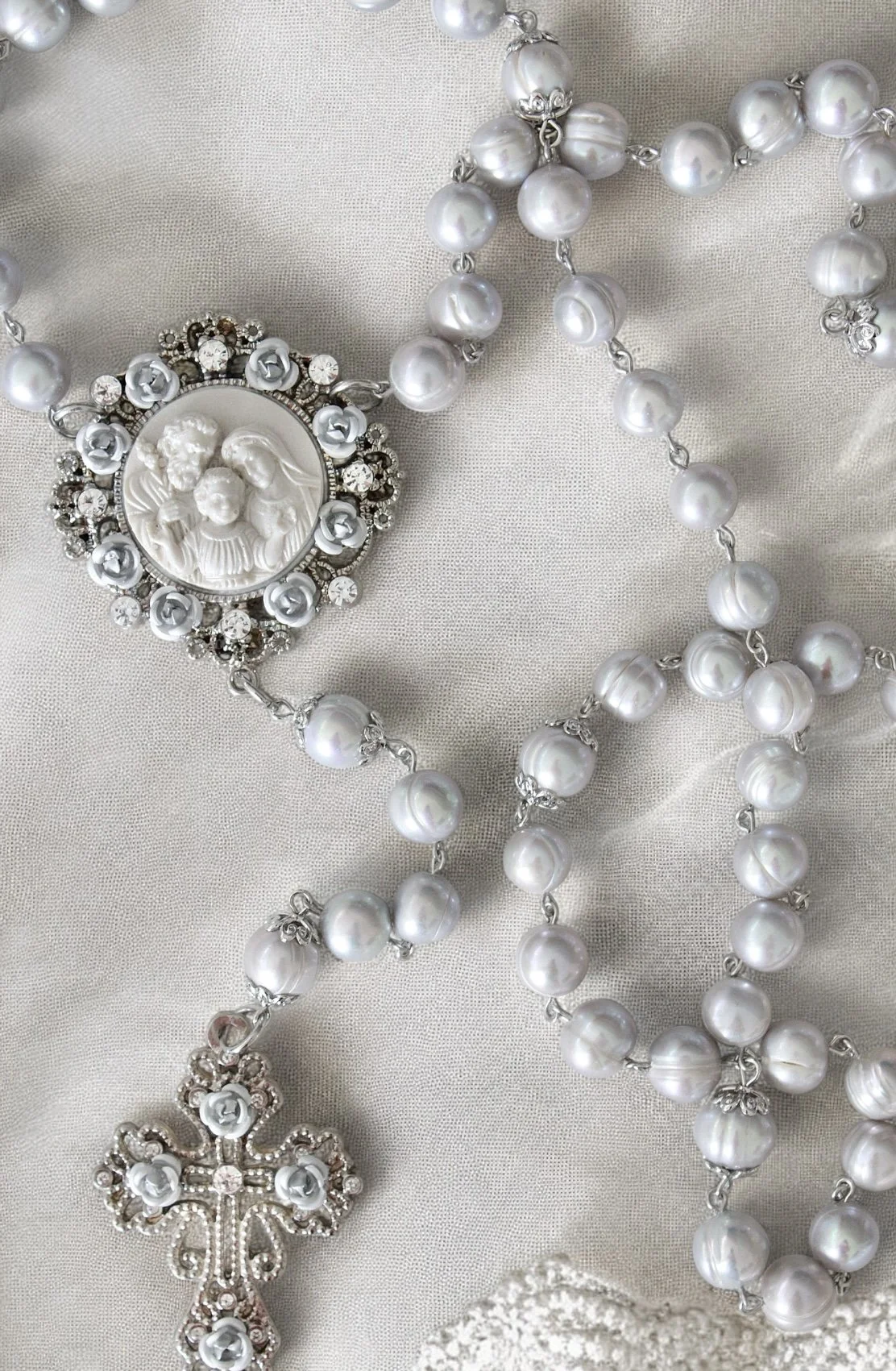 A pearl necklace with a cameo pendant depicting three women and two smaller decorative pendants, all laid on a satin fabric.