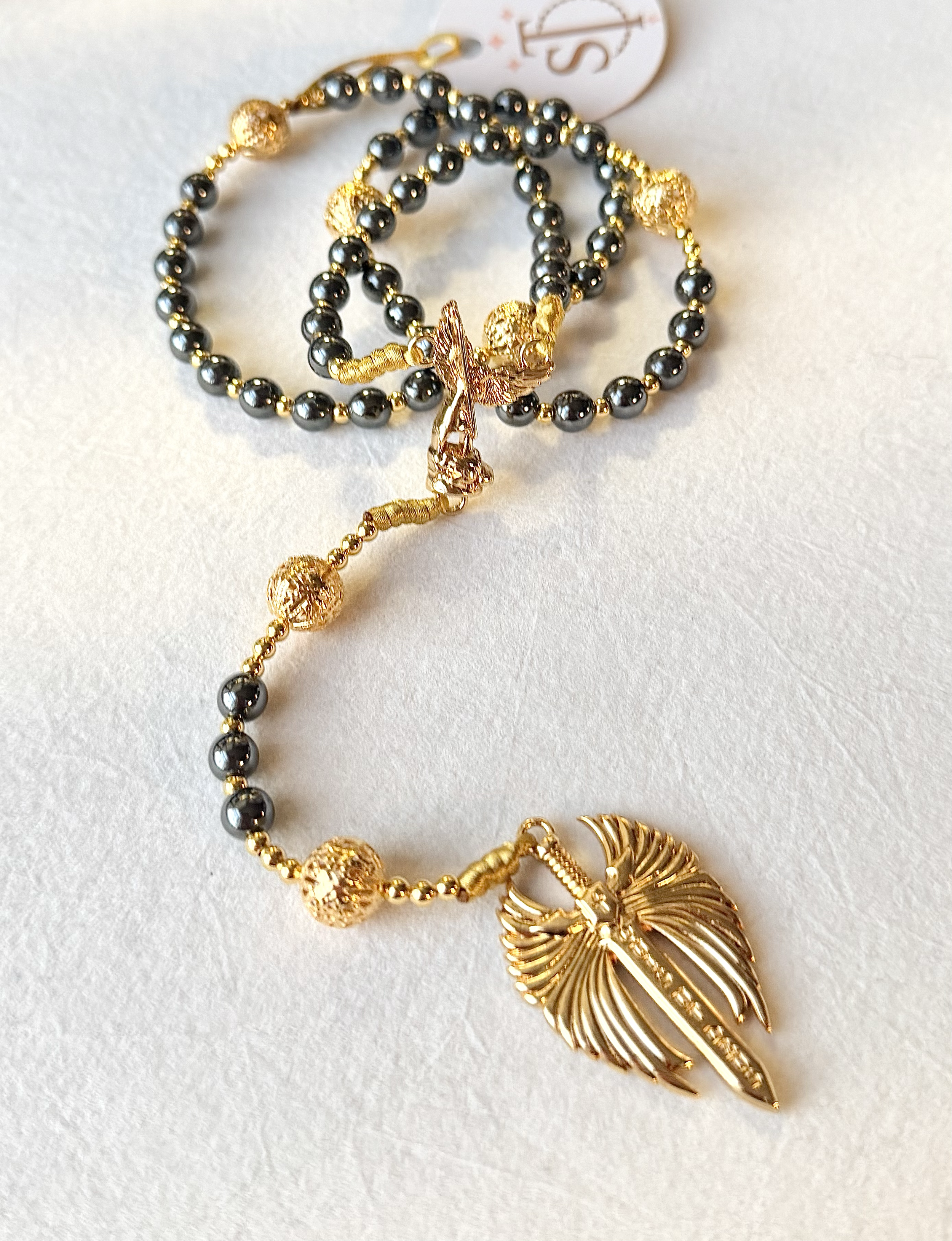 Gold and black beaded jewelry with a gold leaf pendant on a white background.
