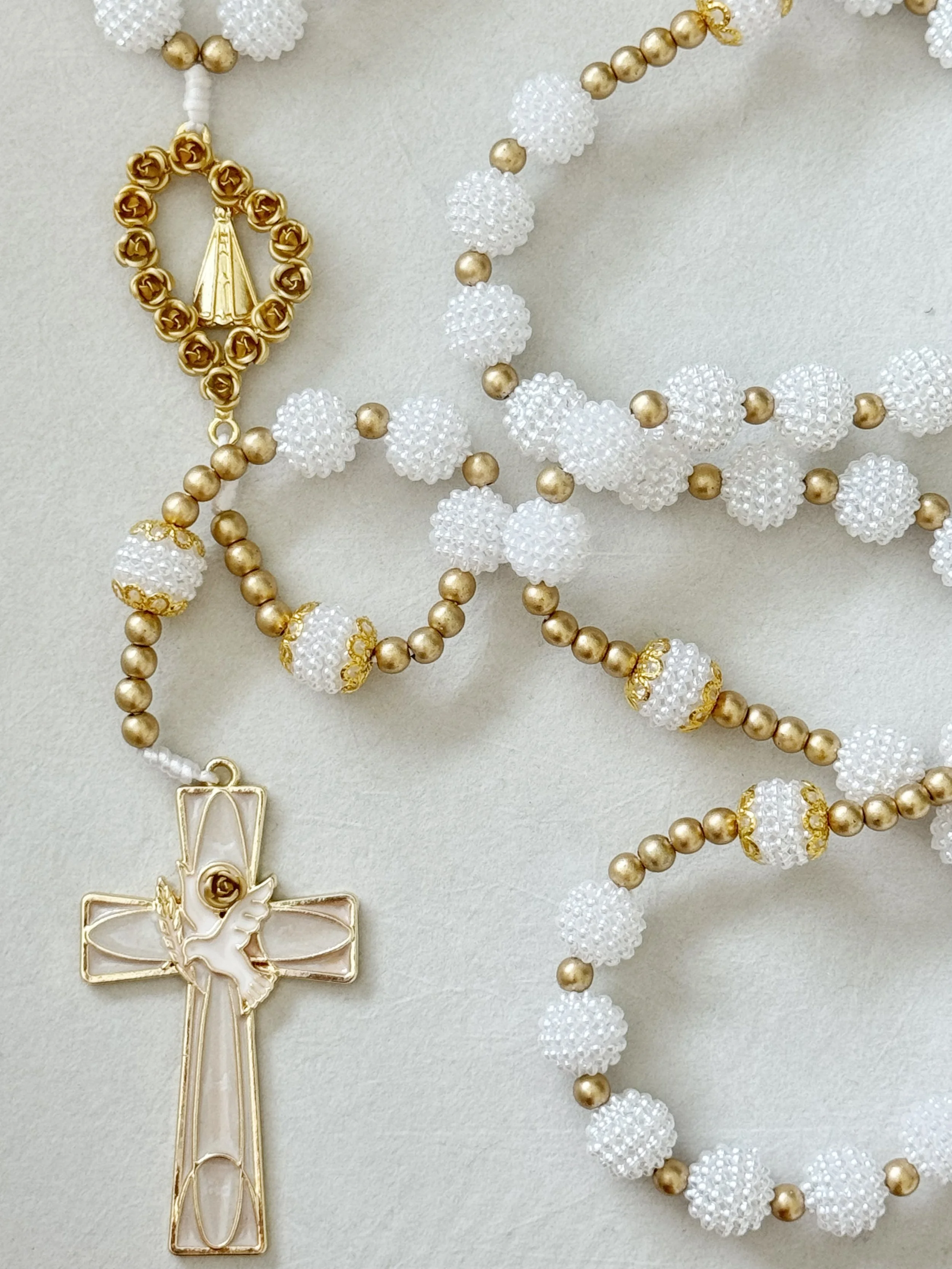 A close-up of a pearl and gold jewelry necklace with a gold and white cross pendant featuring a flower design and a white background.