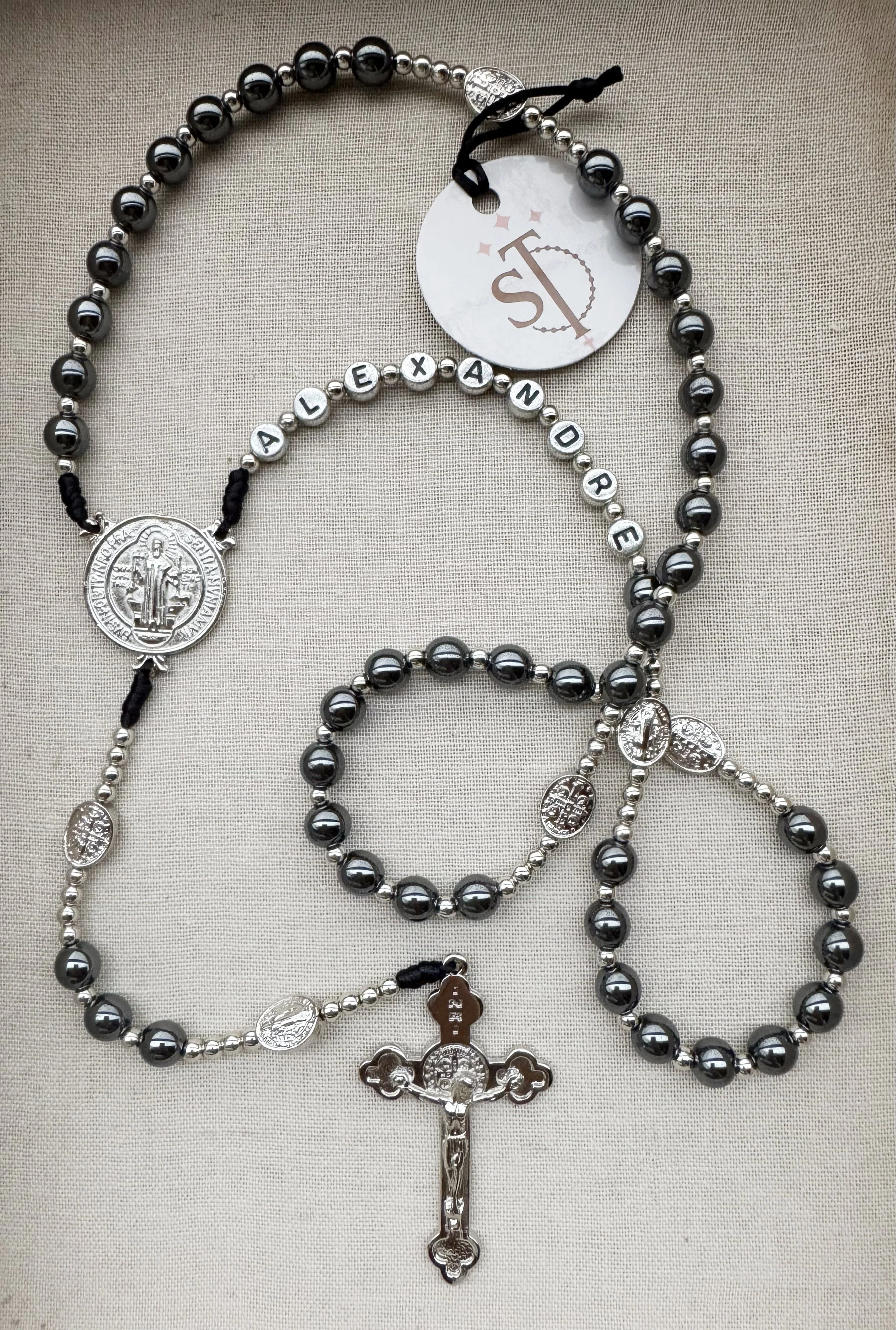 Black and silver beaded rosary with metallic medals and a crucifix, displayed on a beige fabric background