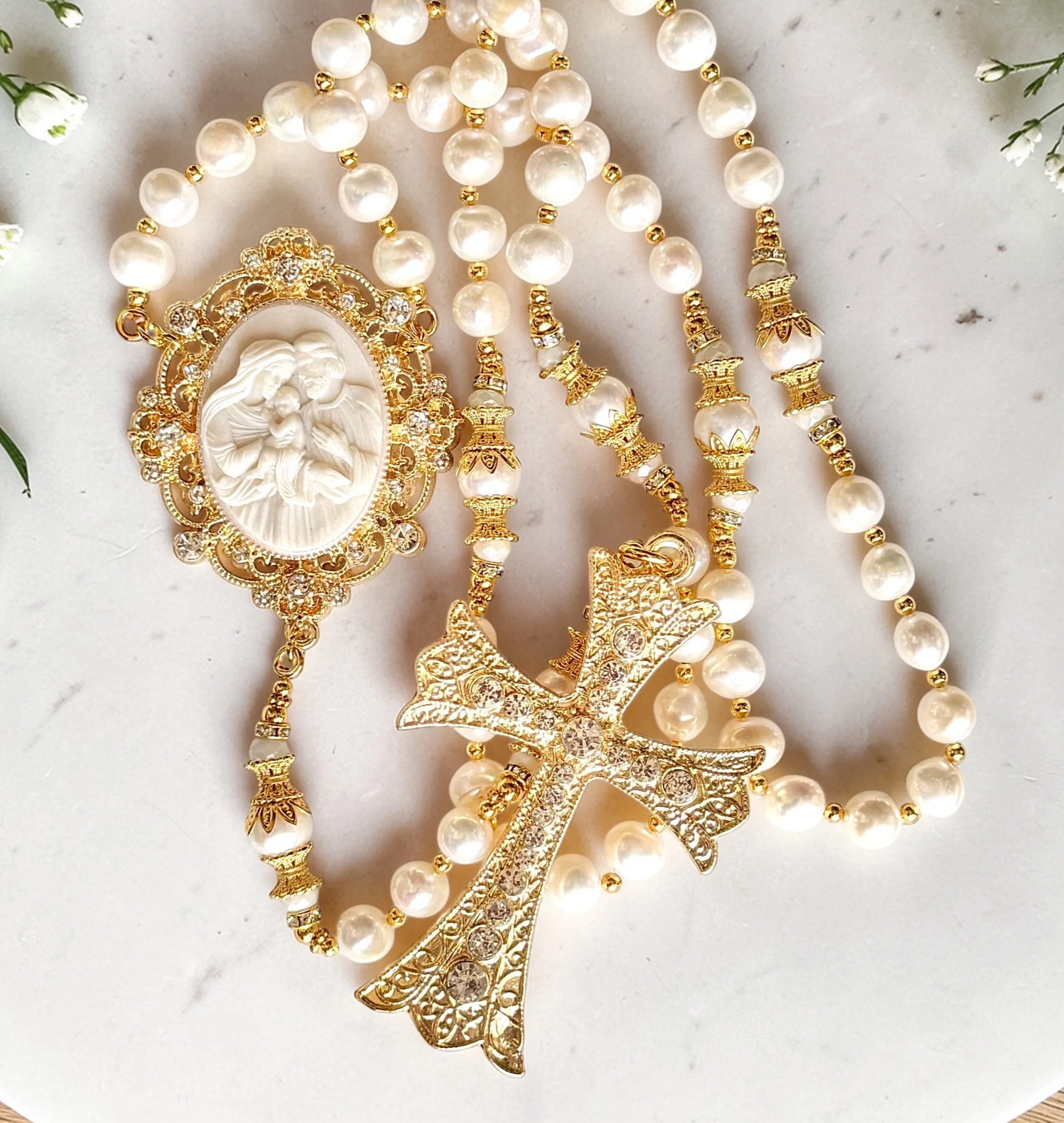 Gold and pearl jewelry, including a pendant with a religious figure and other necklaces with decorative beads and charms, arranged on a light surface.