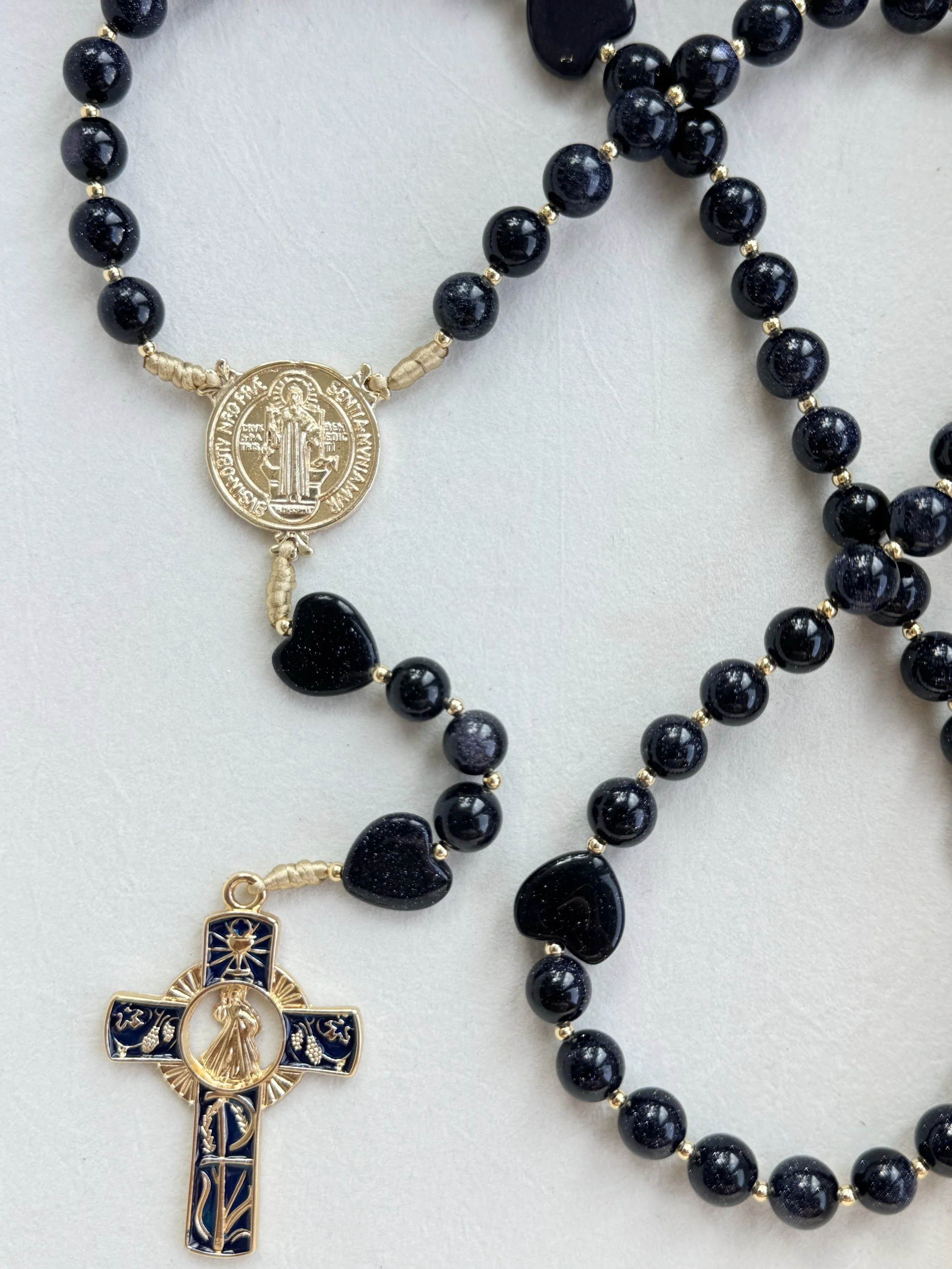 A black bead rosary with gold accents featuring a gold and blue crucifix and a medallion with a religious figure.