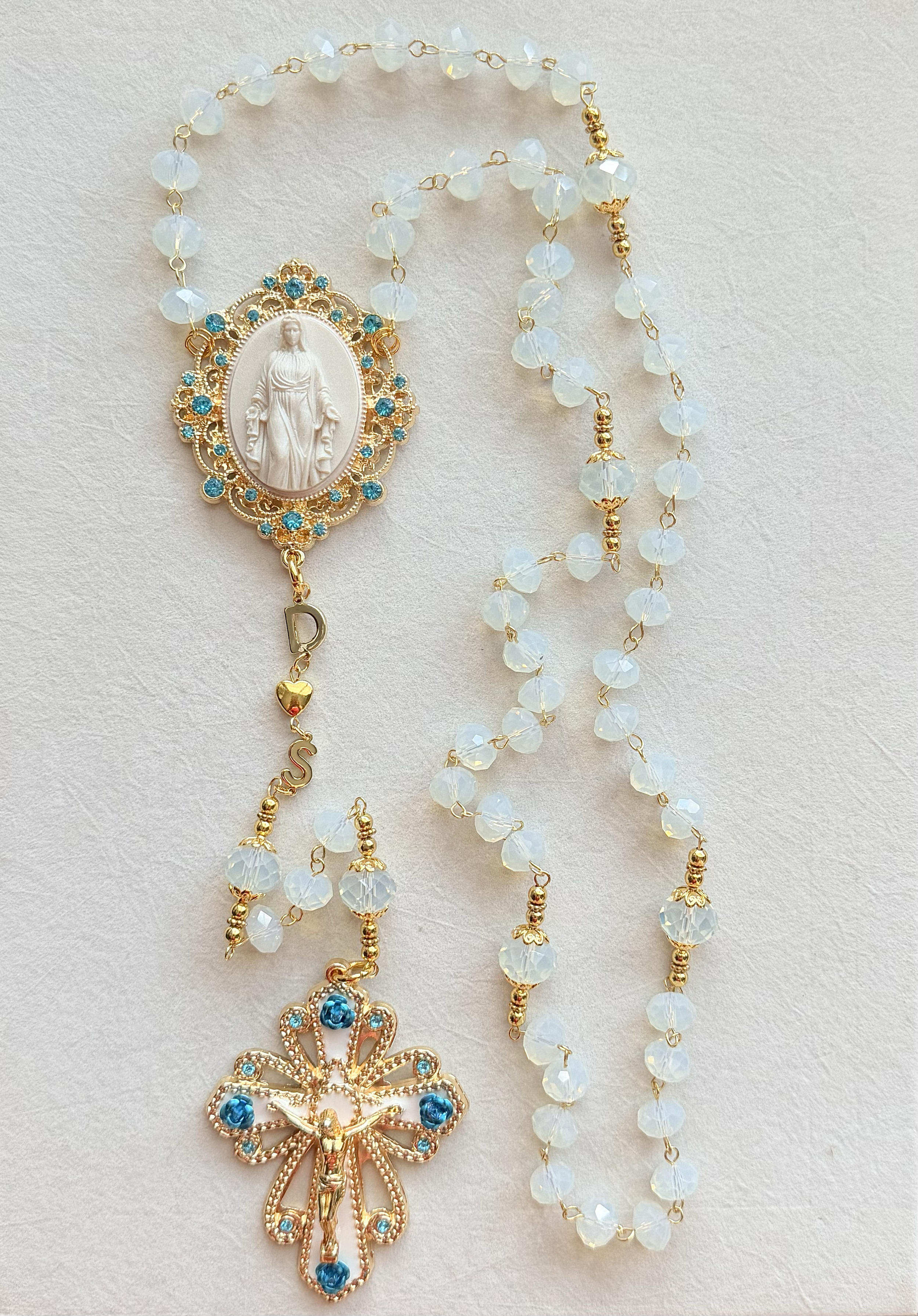 Gold and white rosary with a pendant featuring the Virgin Mary and a bow design with blue accents.