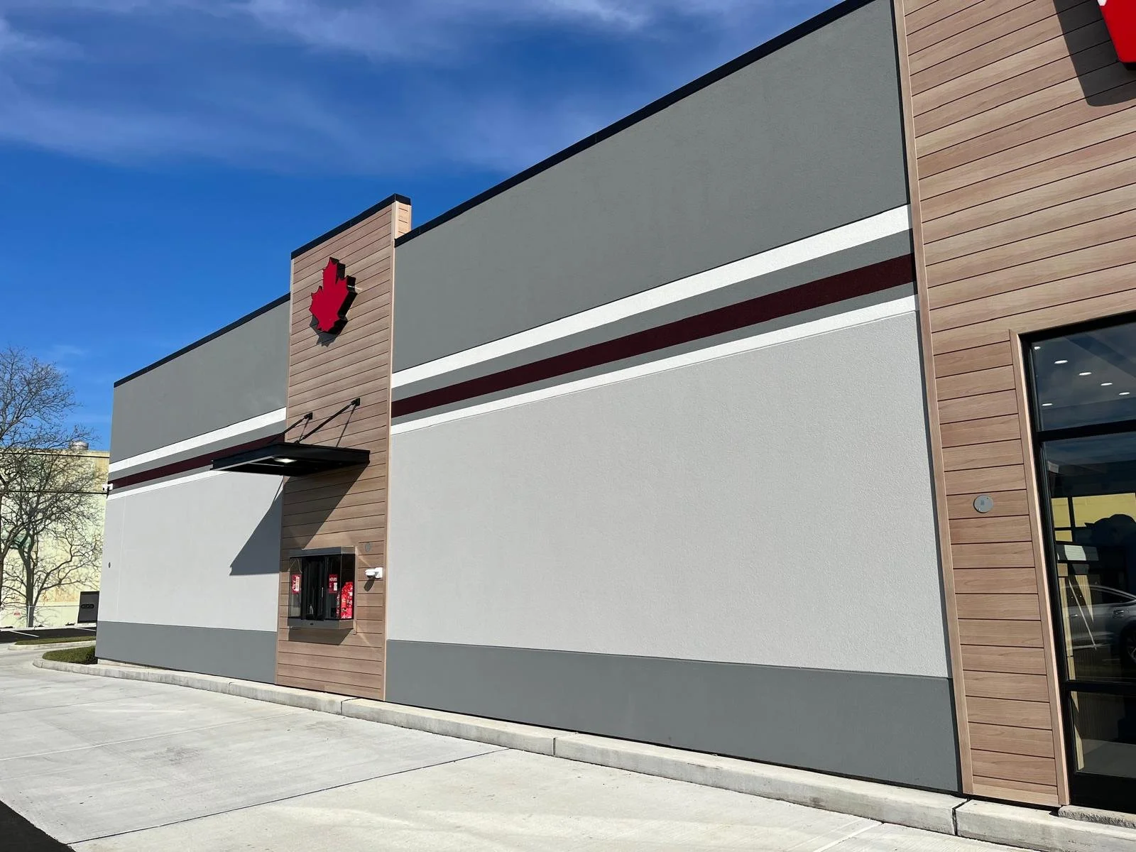 Exterior of a modern white building with wood panel accents, featuring a red maple leaf logo and a fire station box, under a blue sky.