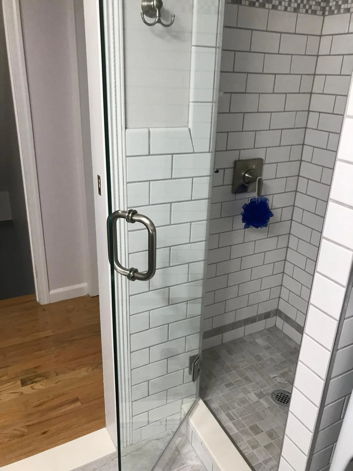 Inside a glass shower with white subway tiles, a silver faucet with a blue loofah hanging, and a floor drain.