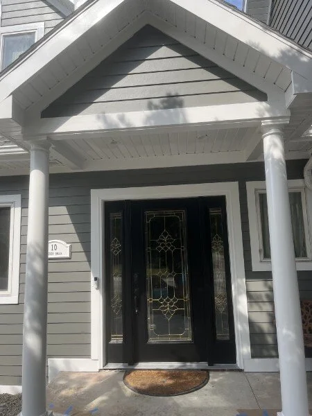 Front entrance of a house with a black door and decorative glass, gray siding, a covered porch with white columns, and house number 10.