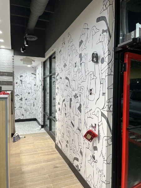 Interior hallway with a black and white abstract line art mural on the wall, a fire alarm, and a red fire extinguisher case.