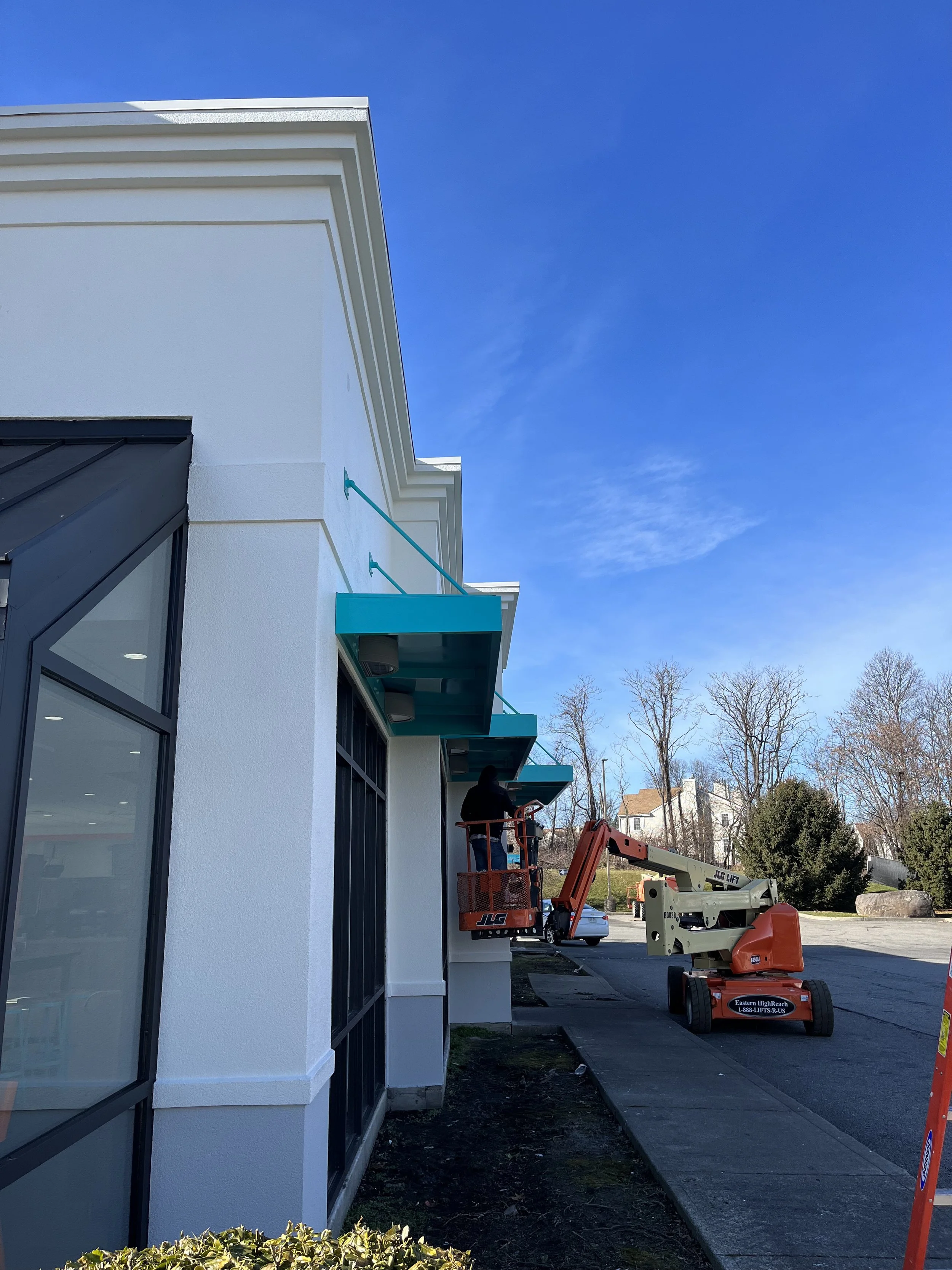 Workers on a lift working on the exterior of a white building with black window frames, under a clear blue sky.
