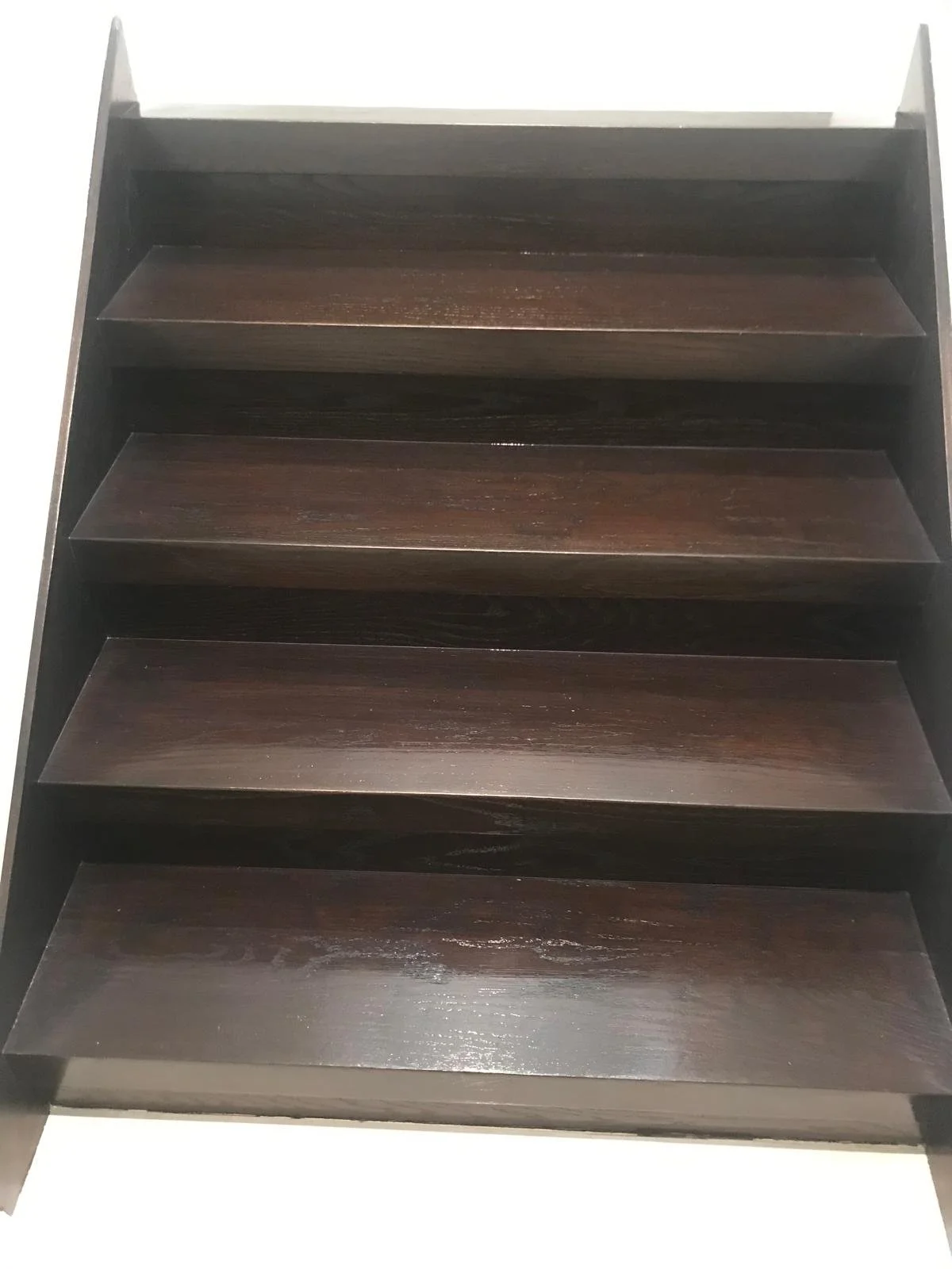 Dark wooden staircase with five steps, viewed from below against a white background.
