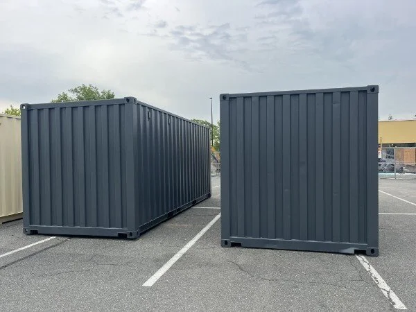 Two large blue shipping containers placed in a parking lot.