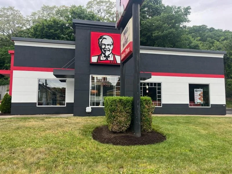KFC fast food restaurant with black, white, and red exterior, featuring the Colonel Sanders logo sign in front.