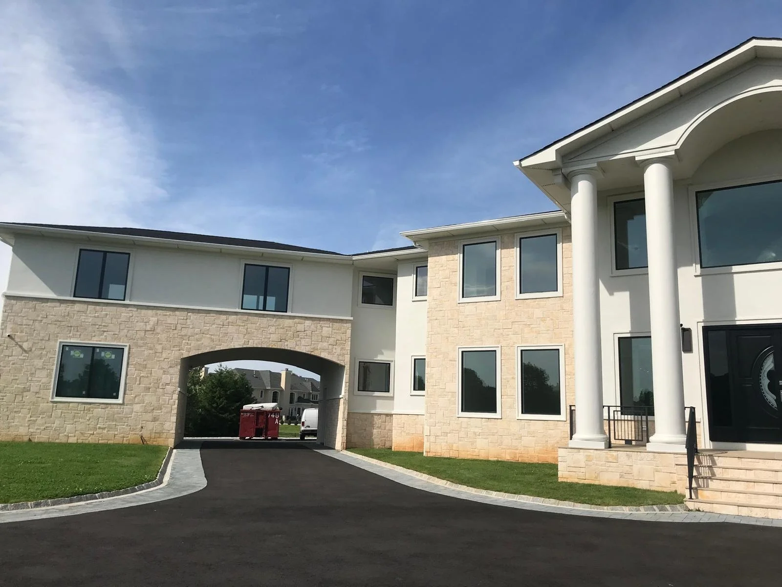 Modern multi-story residential building with stone and white exterior walls, large windows, a driveway, and an archway connecting sections under a blue sky.