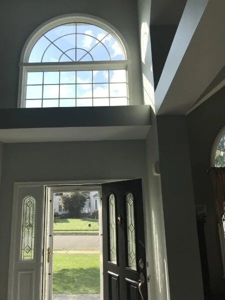 Interior view of a house entryway featuring a large arched window above a front door with sidelights, allowing natural light to illuminate the space.