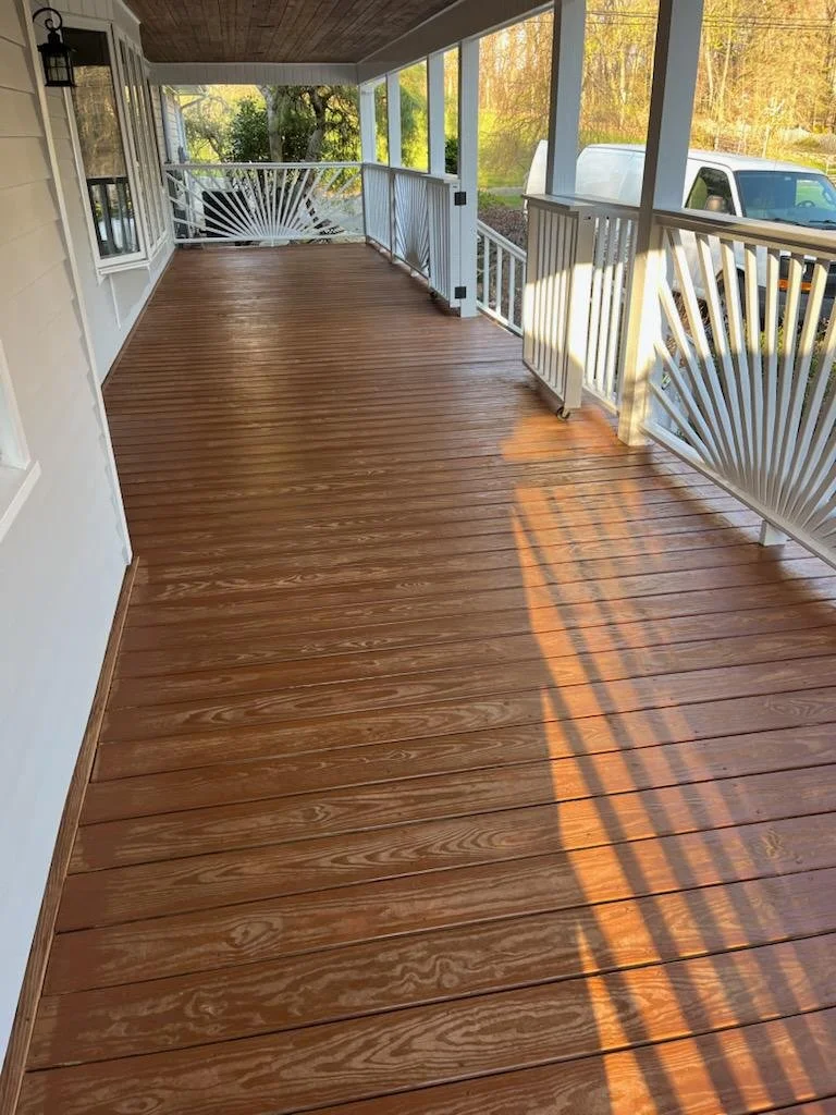 Empty screened porch with polished wood flooring, white railing, and view of trees and vehicles outside.