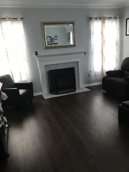 Living room with a fireplace, a large mirror above it, two windows with curtains, and two armchairs.