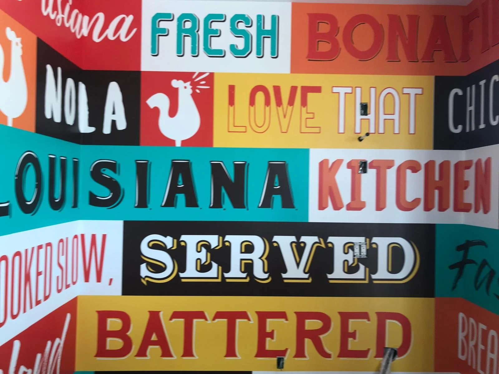 Colorful menu board with various food and drink options written in different fonts and colors, including words like "fresh," "no a," "Louisiana," "served," and "battered."