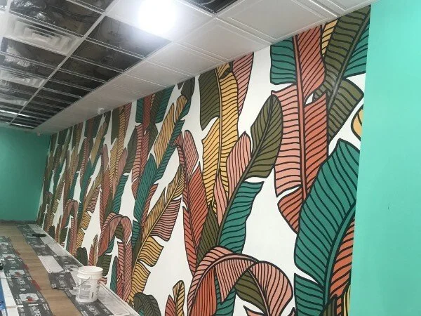 A colorful wall mural featuring large, stylized leaves in green, brown, yellow, and orange hues.