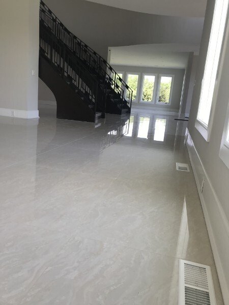 Empty room with shiny, polished light-colored marble floor, large windows, a staircase with black railing, and a white ceiling with a curved section.