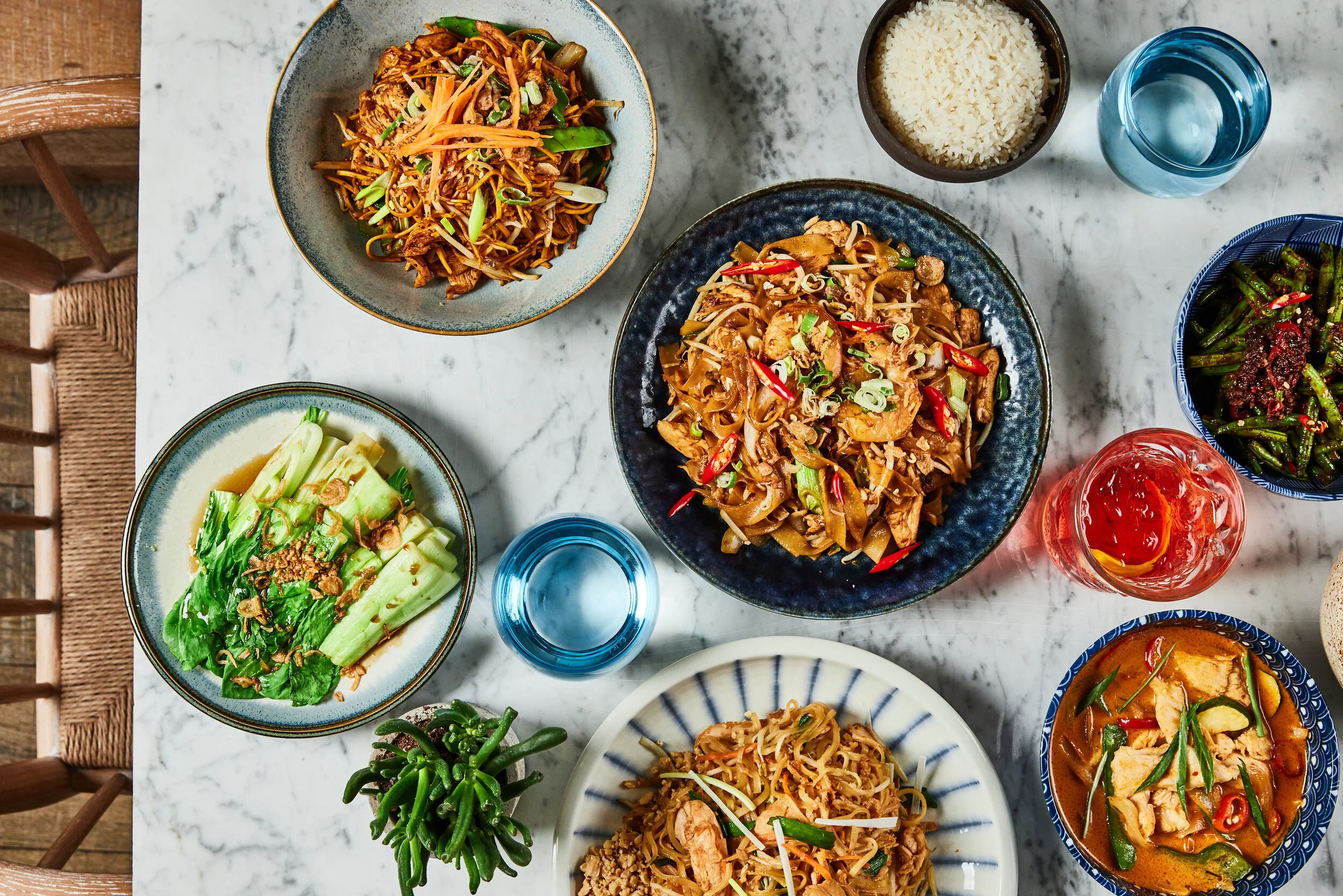 Overhead view of food at HUŎ Asian Restaurant with stir-fried noodles, rice, curry, vegetables, and colorful drinks on a marble table