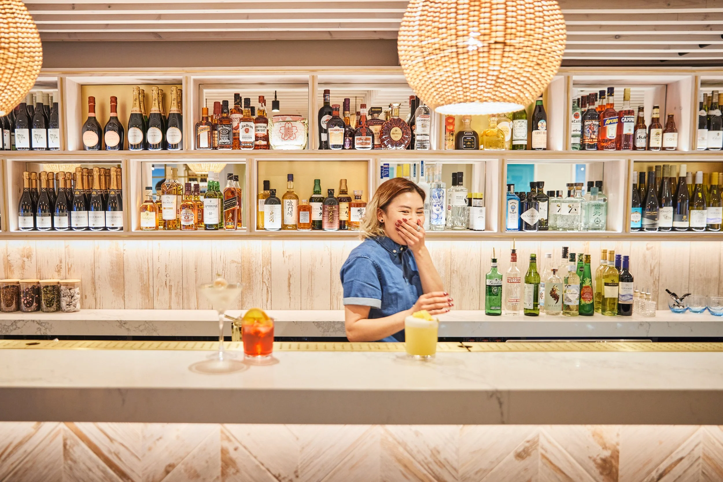 Bartender standing behind a bar with cocktails and shelves of liquor bottles