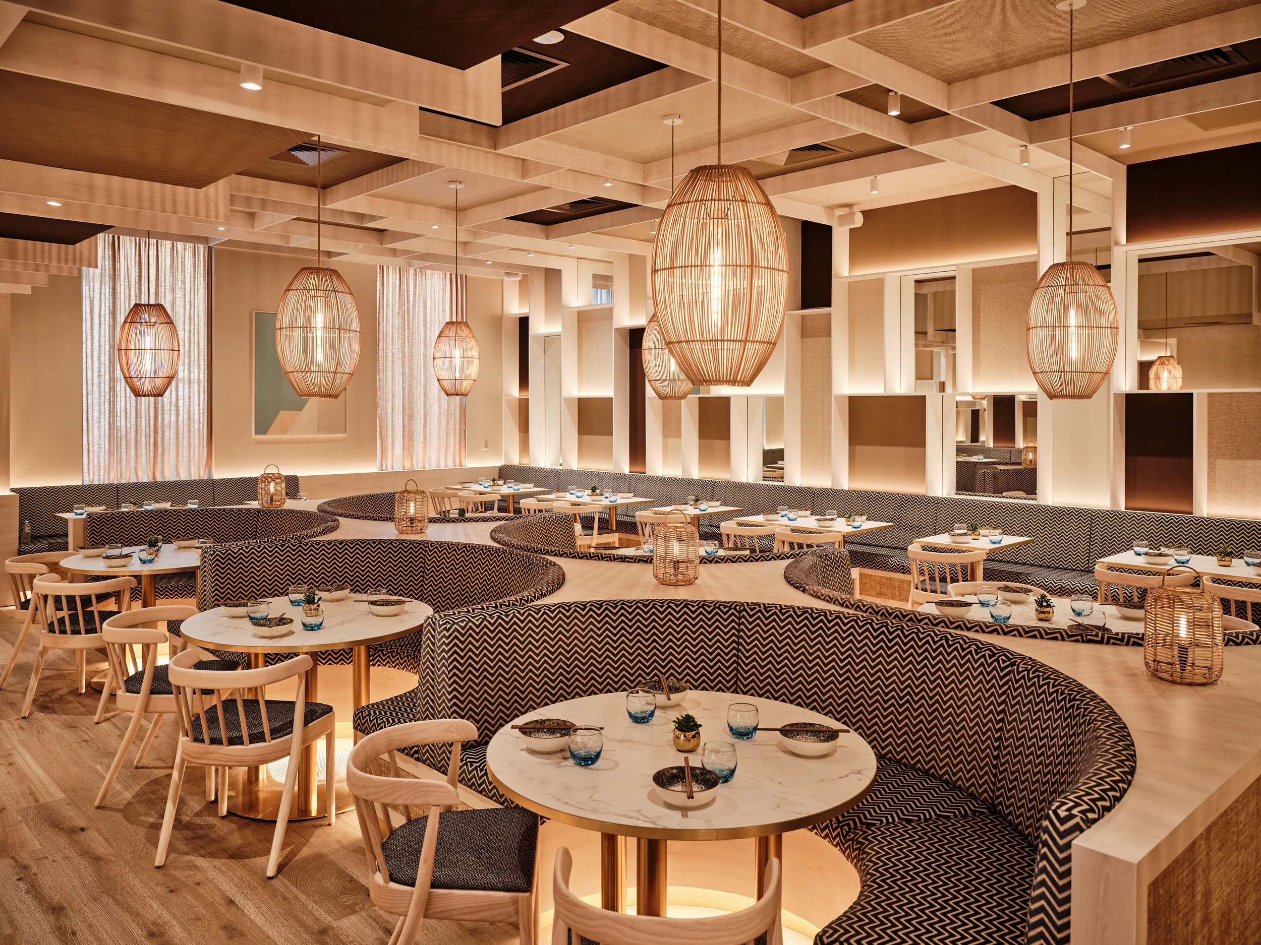 HUŎ Belsize Village dining room interior with patterned banquettes, marble dining tables, woven pendant lights, and warm wood-and-cream decor