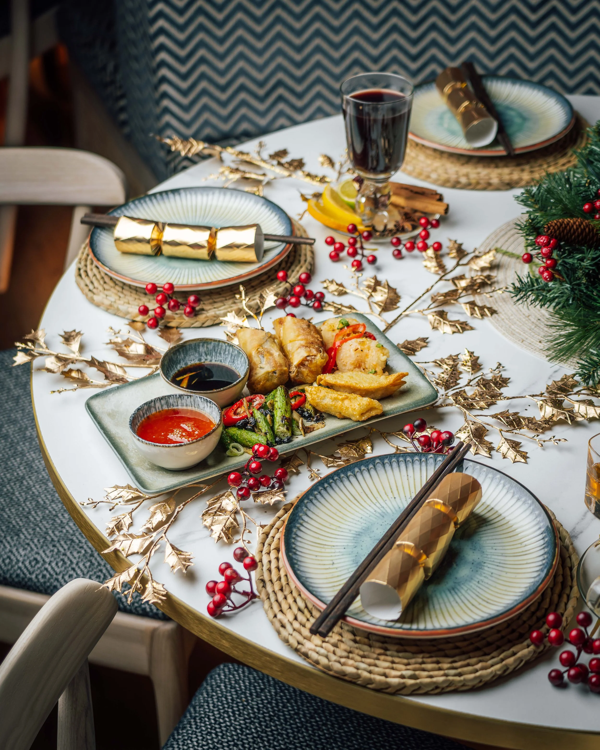 Festive holiday dinner table at HUŎ with Asian appetizers, dipping sauces, red wine, gold crackers, berries, and evergreen decorations
