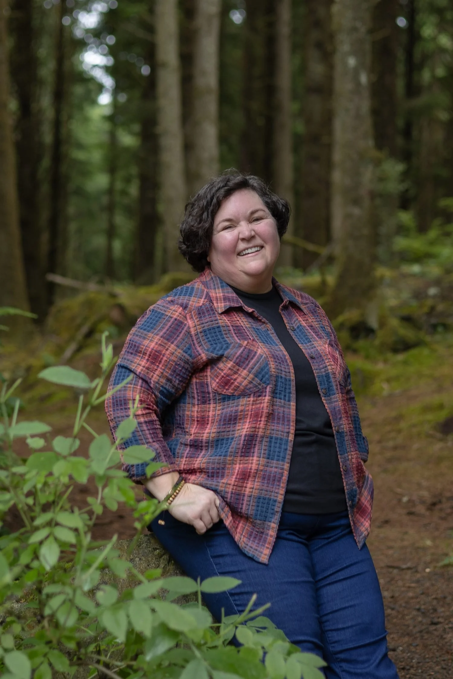 Smiling woman in a plaid shirt standing in a mossy forest