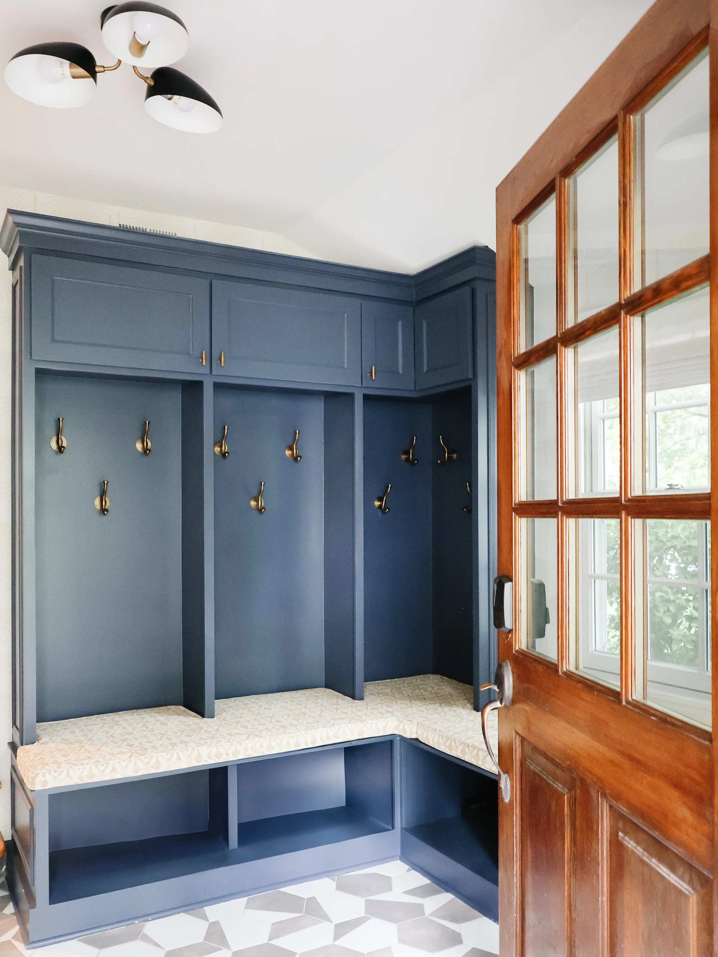 Blue entryway bench with hooks and storage cubbies next to a wooden door with glass panels inside a home.