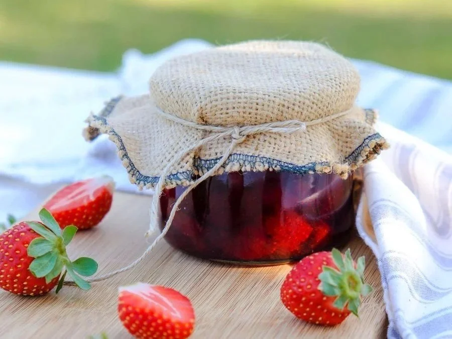 Jar of homemade strawberry jam with fresh strawberries