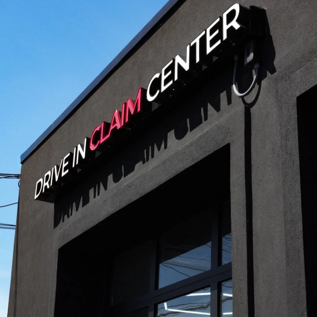 Sign for Drive-In Claim Center on the dark exterior wall of a building, under a clear blue sky.