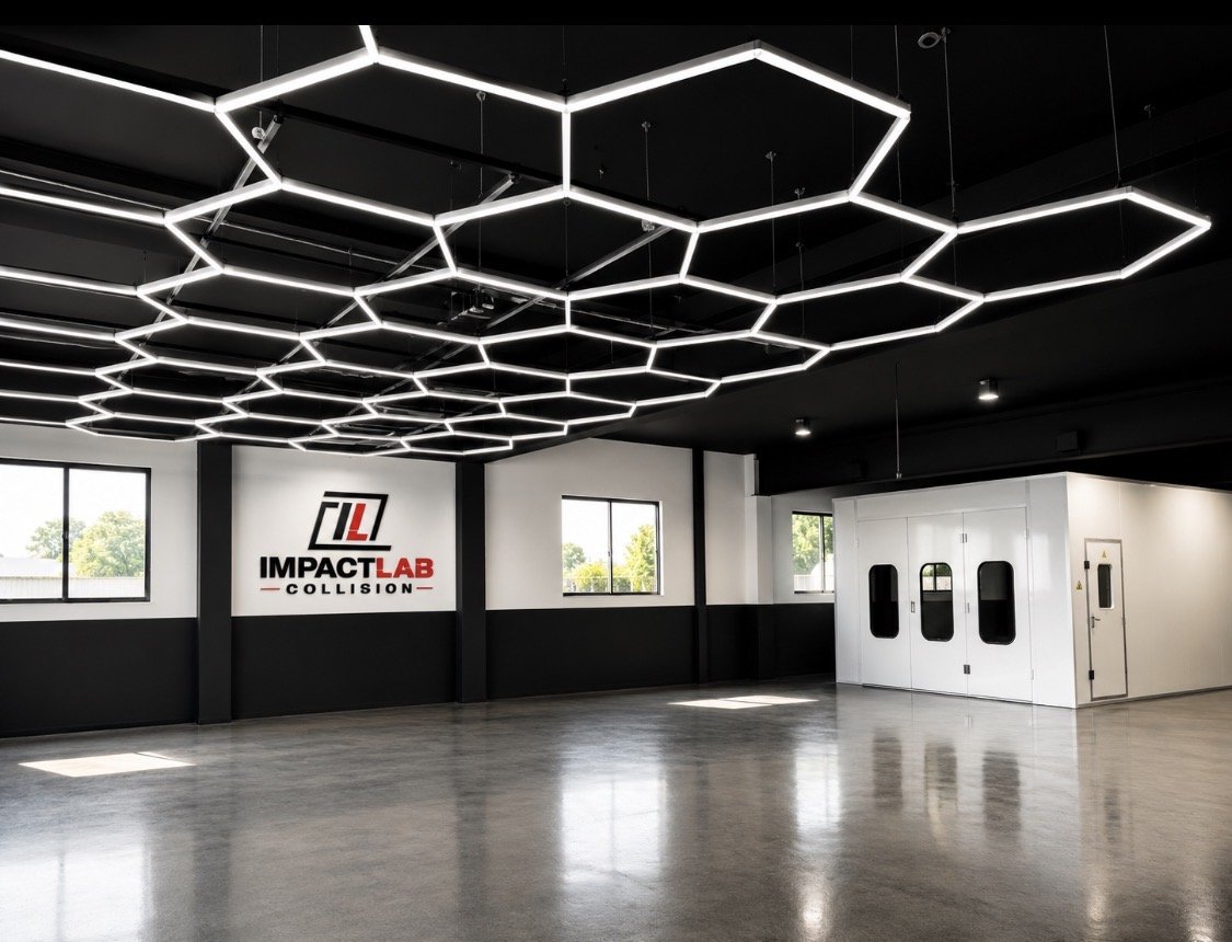 Modern collision repair shop with black and white walls, illuminated hexagonal ceiling lights, windows showing trees outside, a sign reading 'Impact Lab Collision' on the wall, and a white enclosed room with doors.