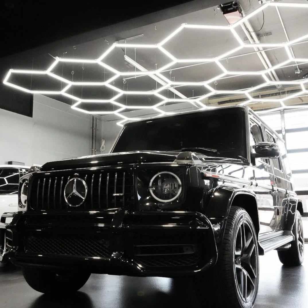 A black Mercedes-Benz G-Class SUV in a modern showroom with geometric LED ceiling lights.