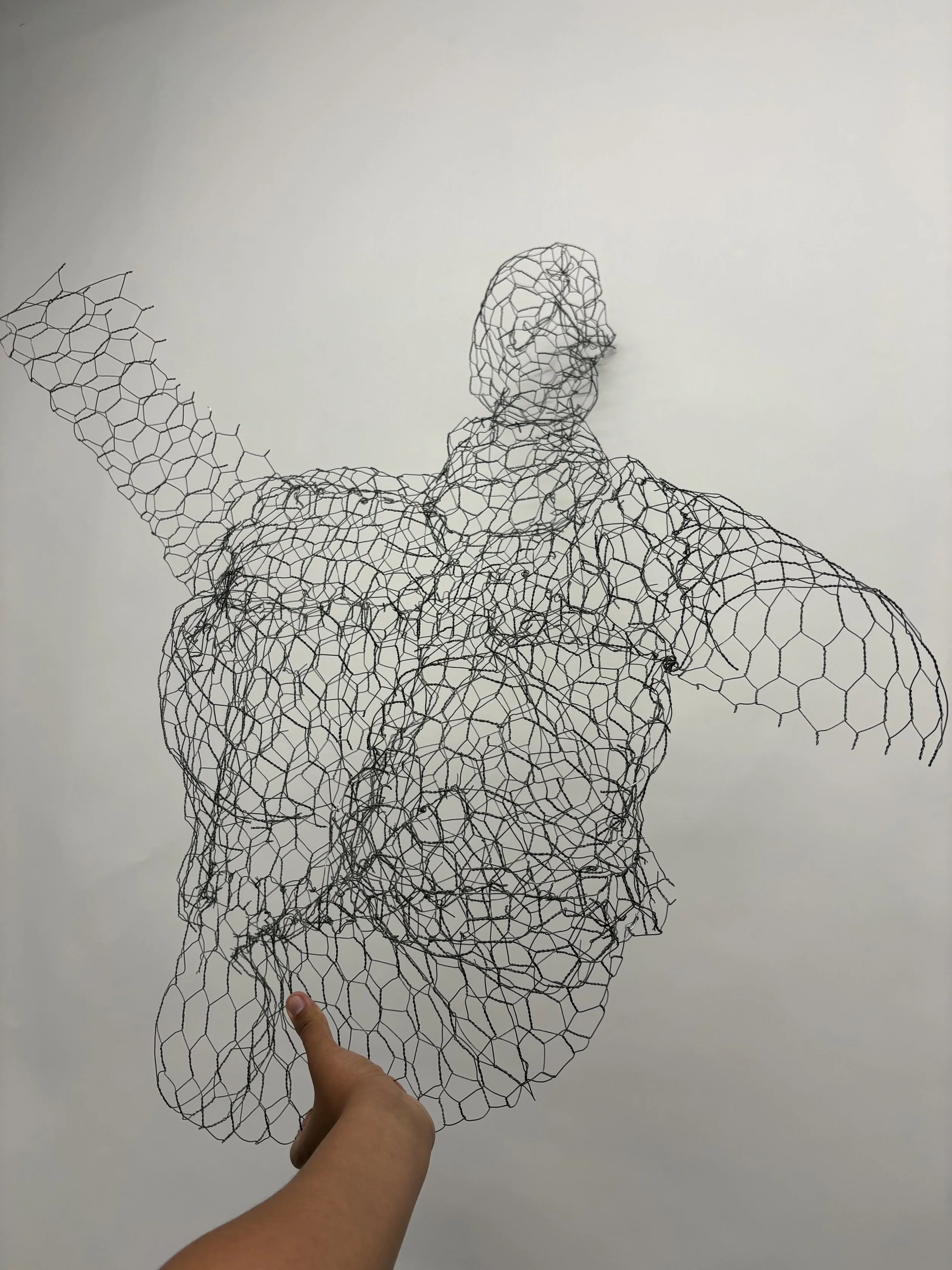 A person's hand holding a wire sculpture of a human figure against a plain wall.