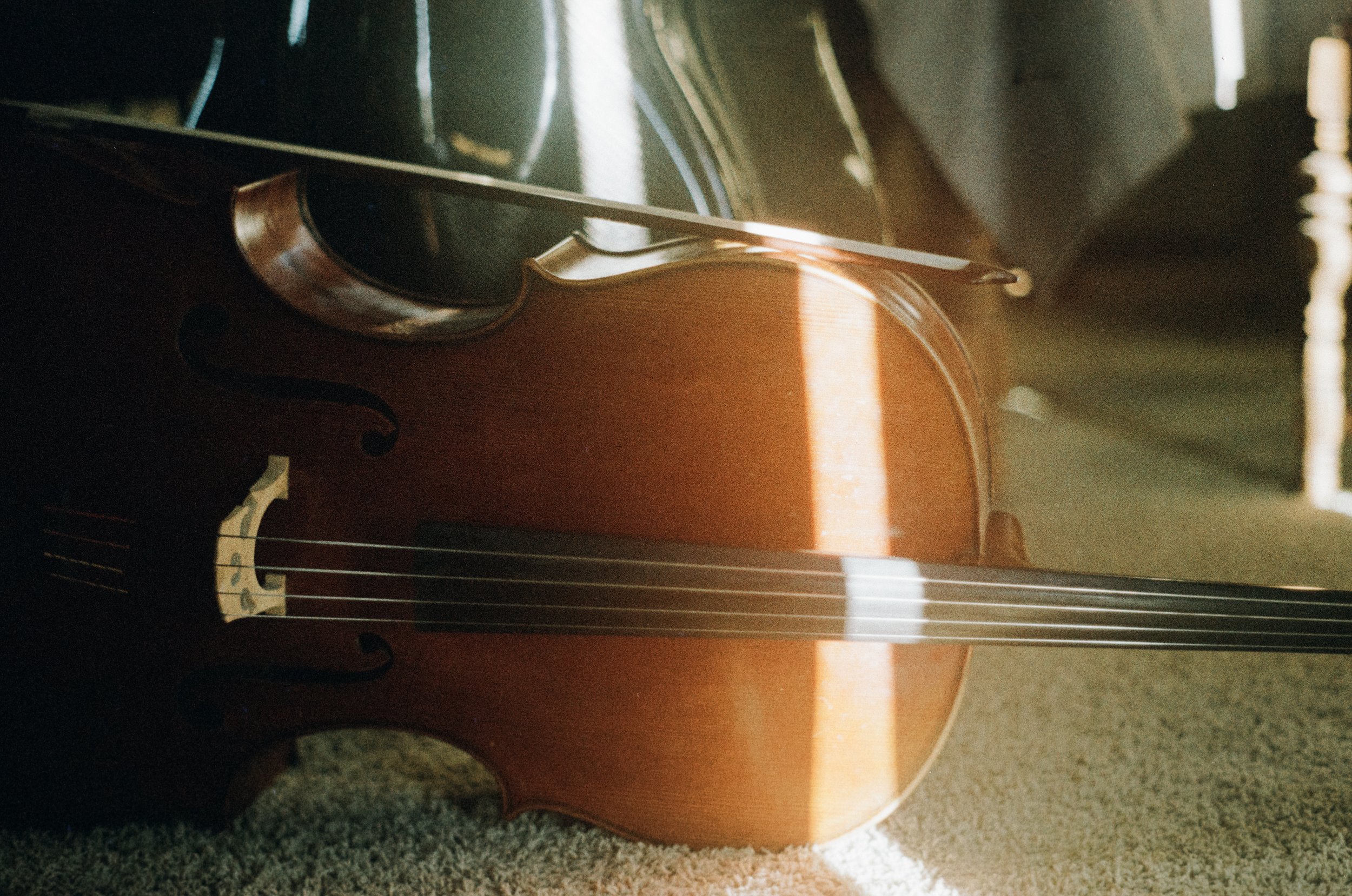 Close-up of a classical acoustic guitar resting on a carpeted floor with sunlight casting shadows on the instrument.