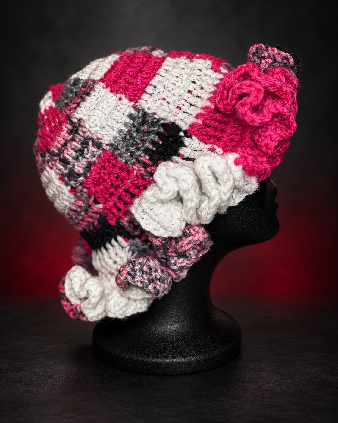 Colorful crocheted hat with pink, white, black, and gray patches on a black mannequin head.
